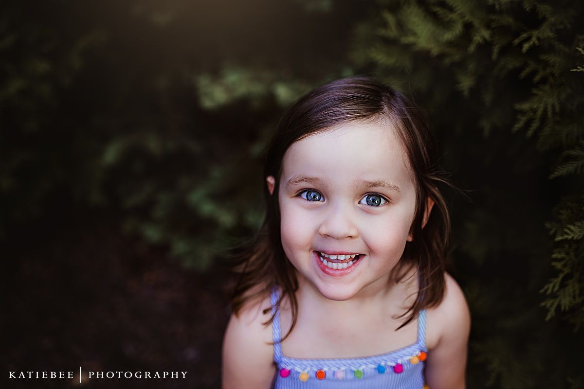 A joyful child smiles brightly while wearing a blue floral dress outdoors.