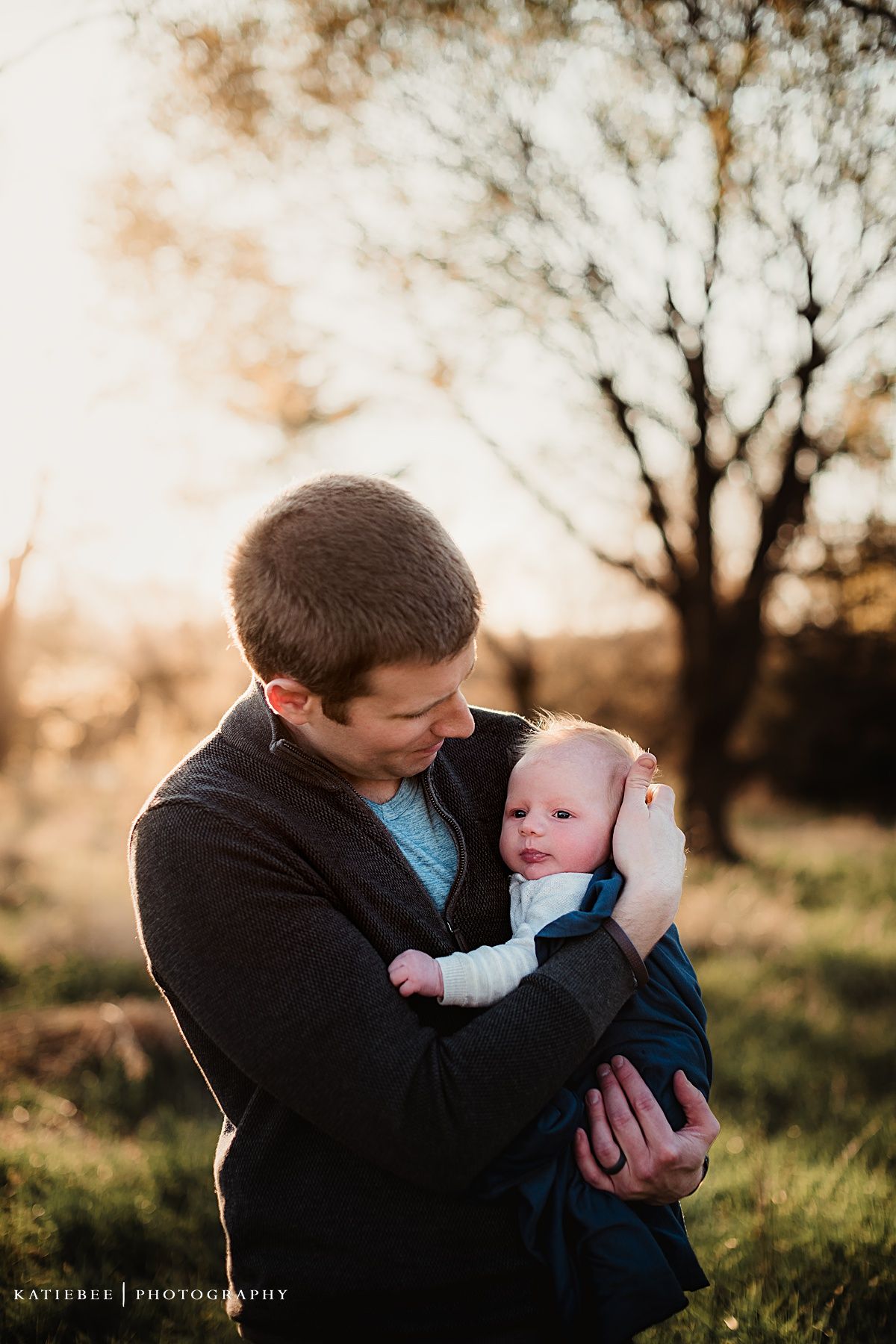 Intimate parent-child portrait captured against sunset sky and bare trees.