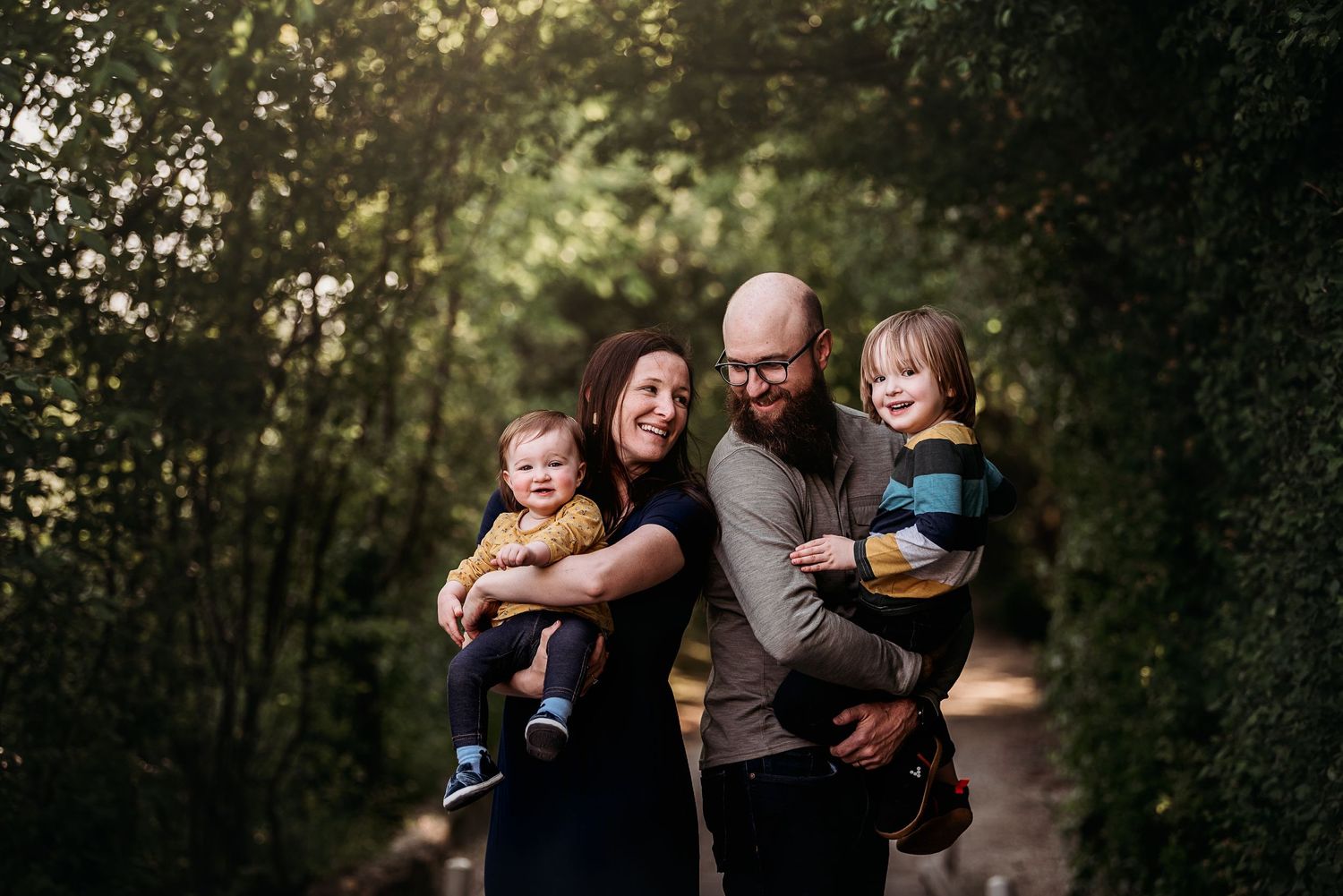Family of four sharing a joyful moment together on a wooded path.