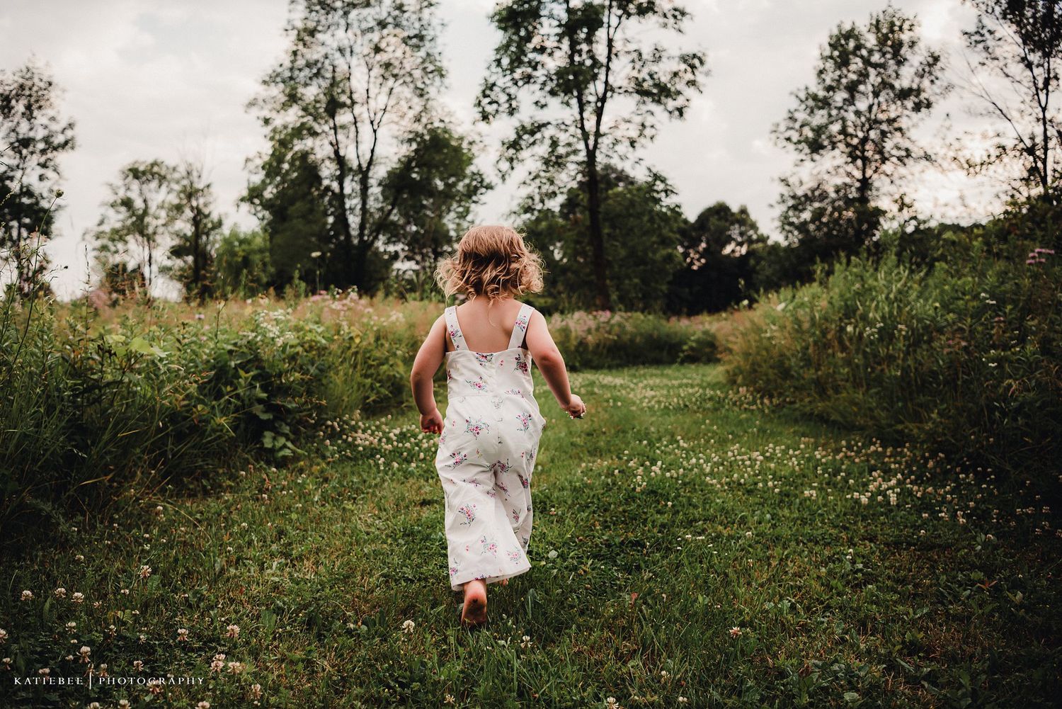 A child in a white dress runs joyfully through a grassy meadow.