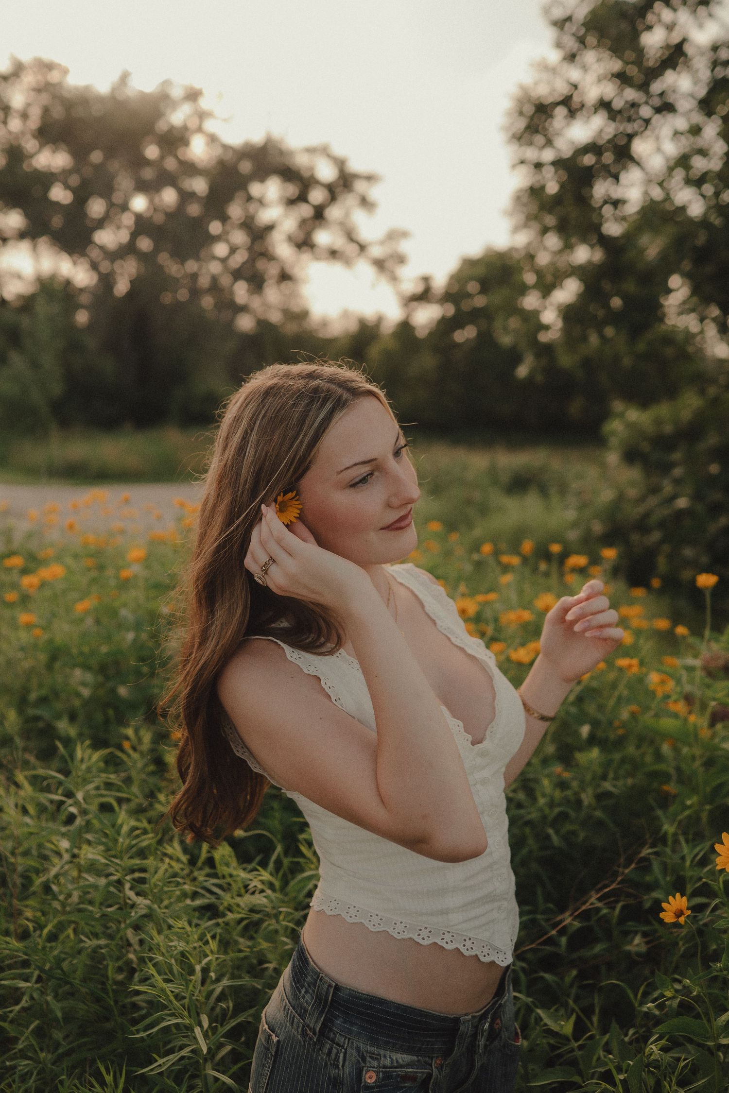 Young woman placing orange flower in hair among golden wildflowers at sunset.