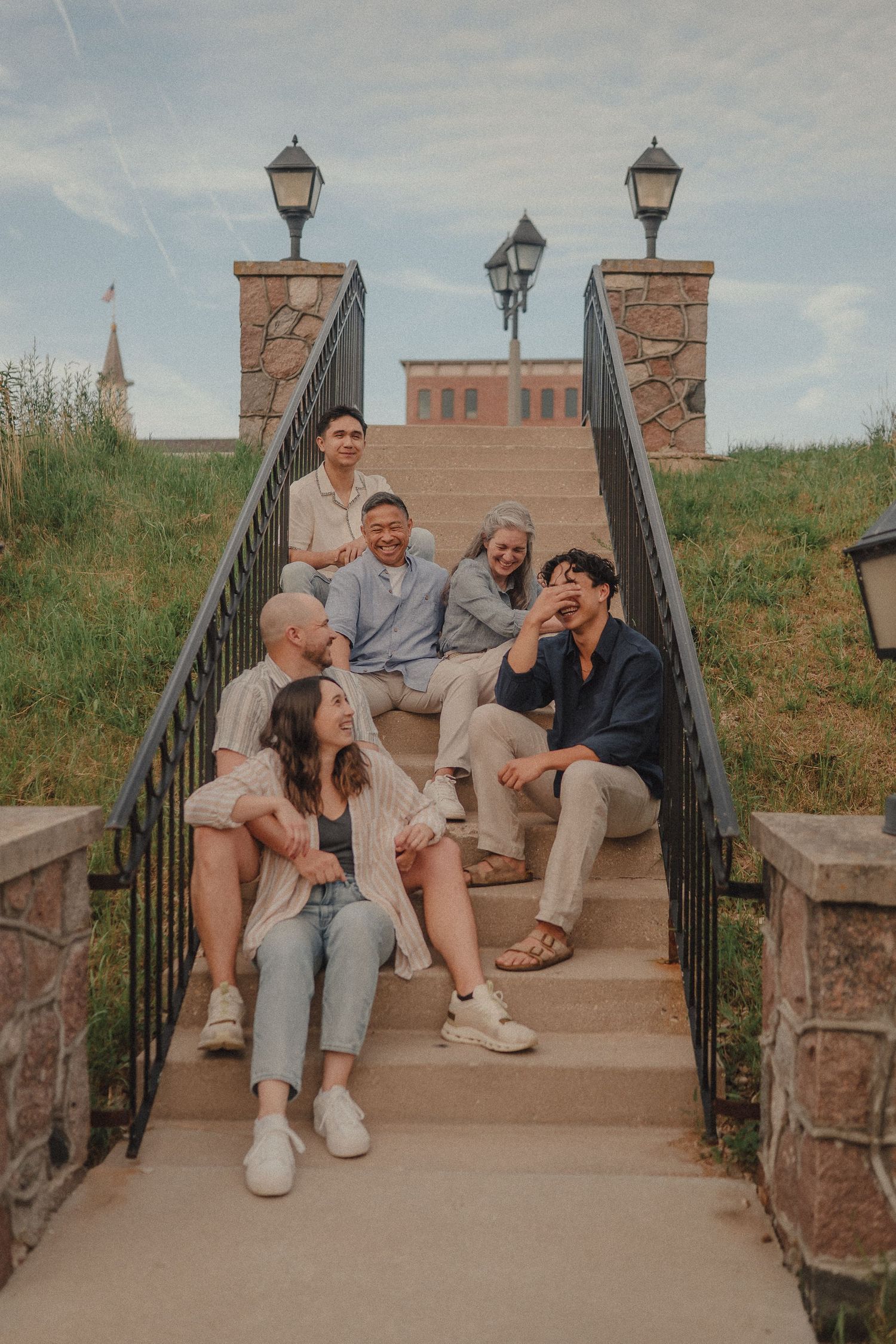 Family of six relaxing on outdoor stone steps with brick buildings and lamp posts behind them.