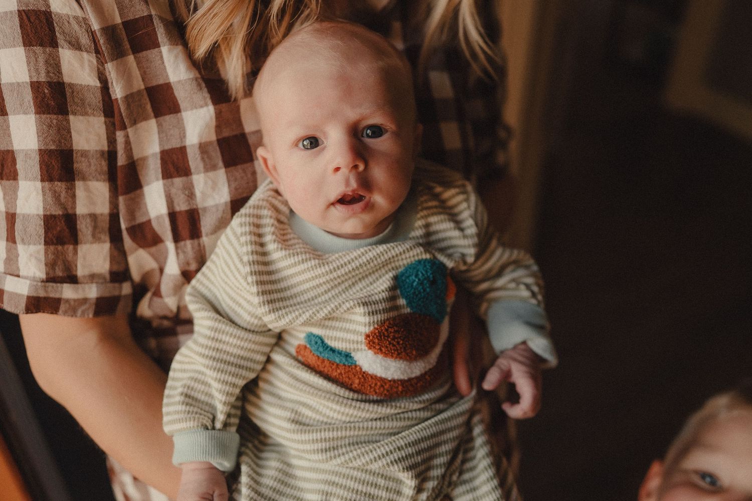 Close-up of an alert newborn baby in a striped onesie with a colorful crochet patch being held by a parent.