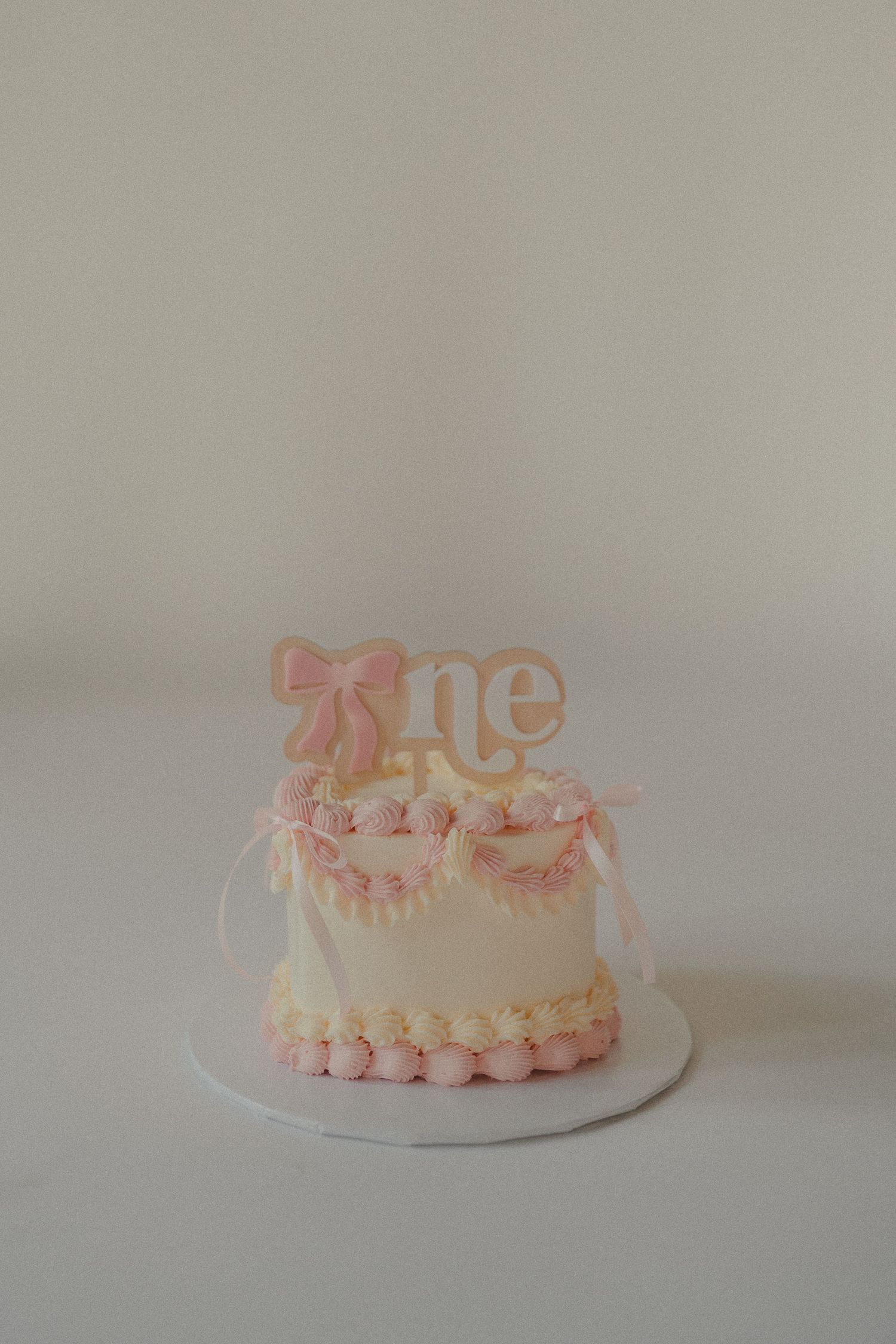 An elegant first birthday cake decorated with pink bows and the word one on a clean white background.