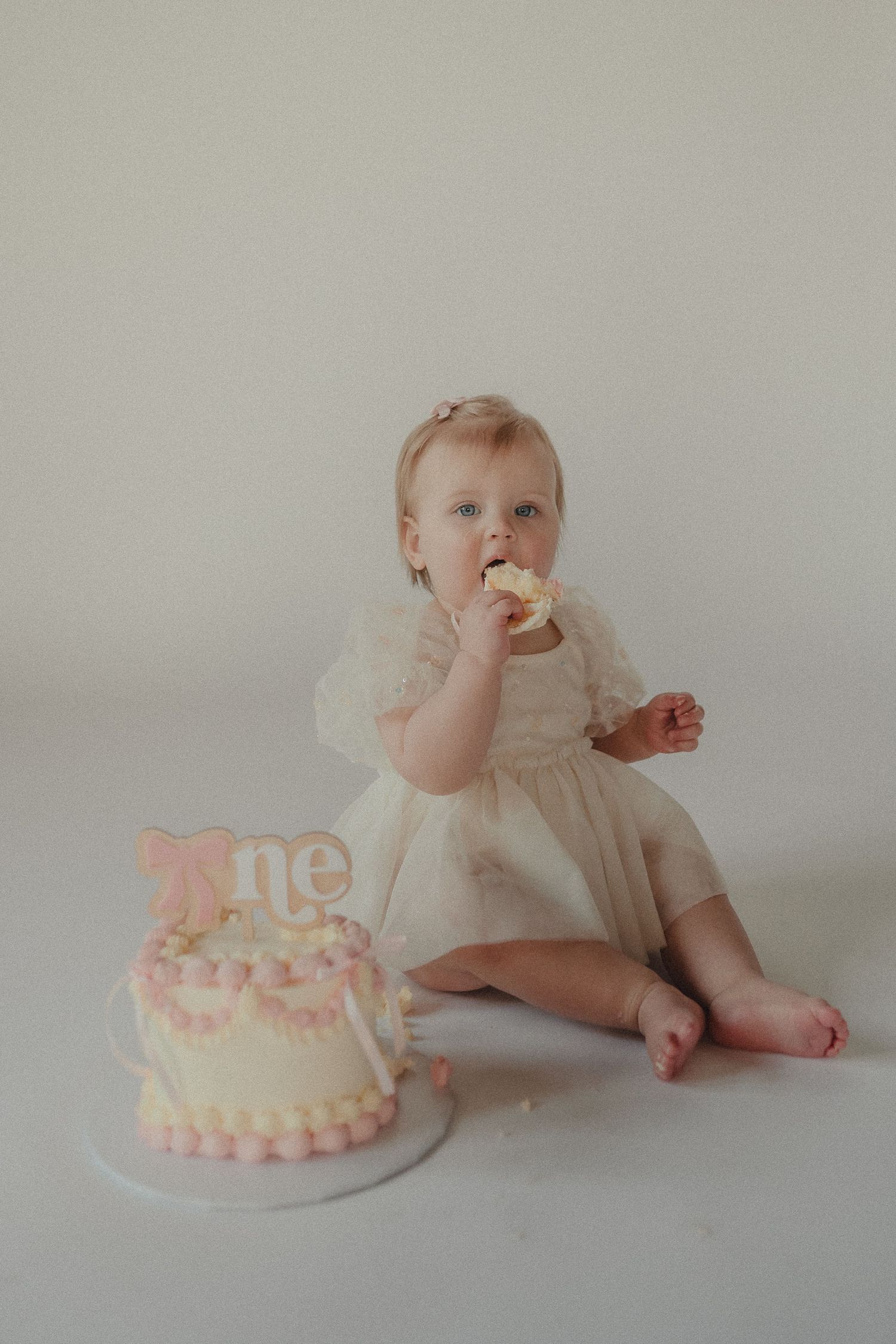 Baby girl in white tulle dress eating cake during her first birthday smash cake photoshoot.
