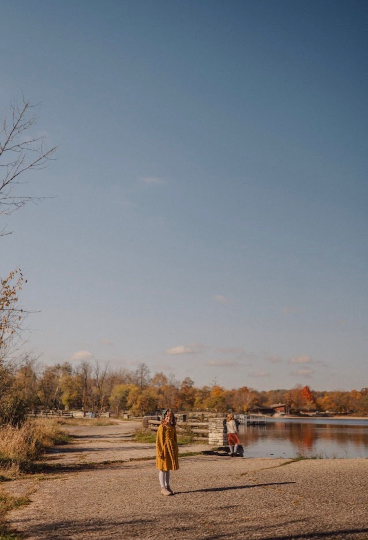 People walking along a lakeside trail during autumn with golden trees in the background.