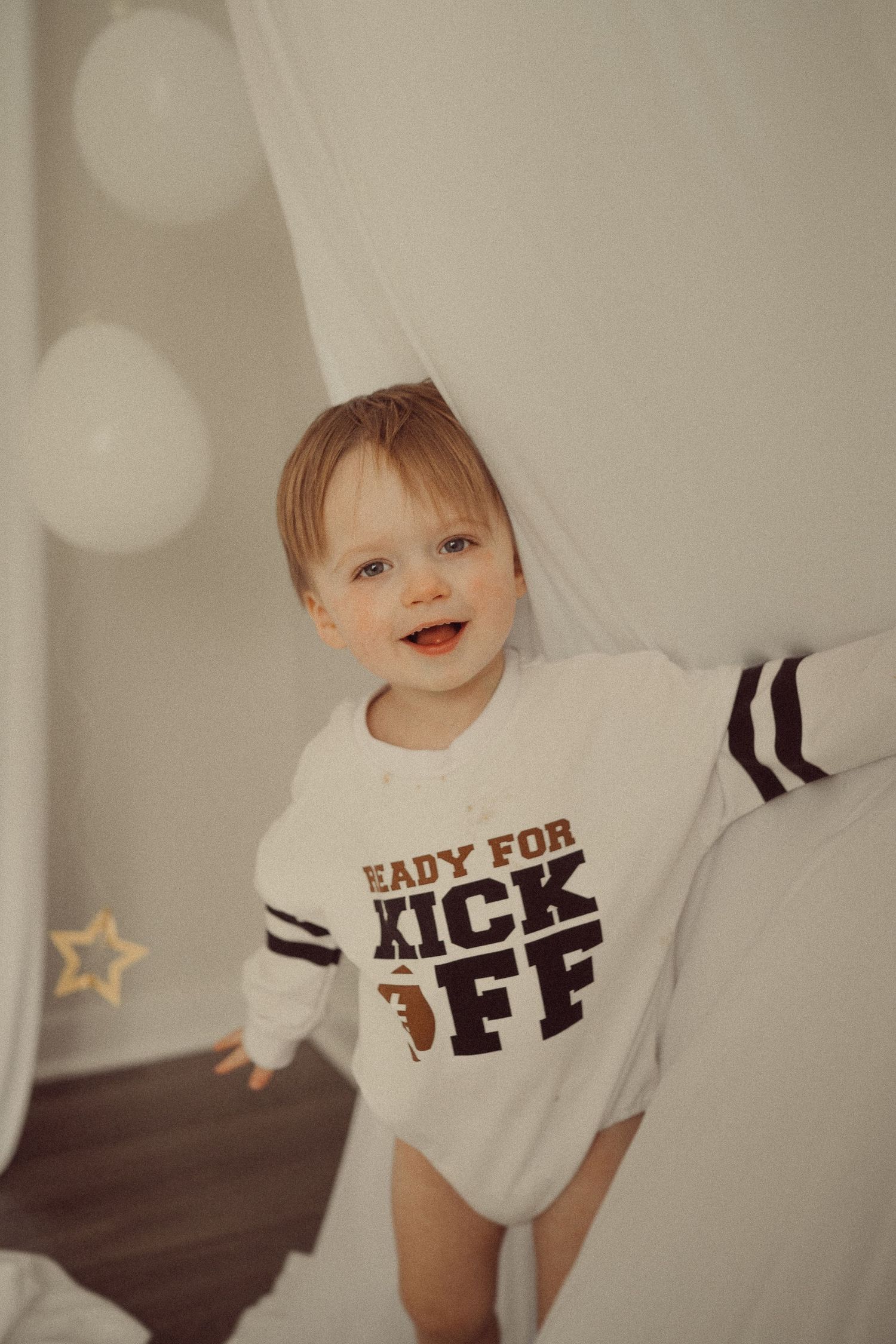 Young child in white football themed onesie smiling against white backdrop with star decorations.