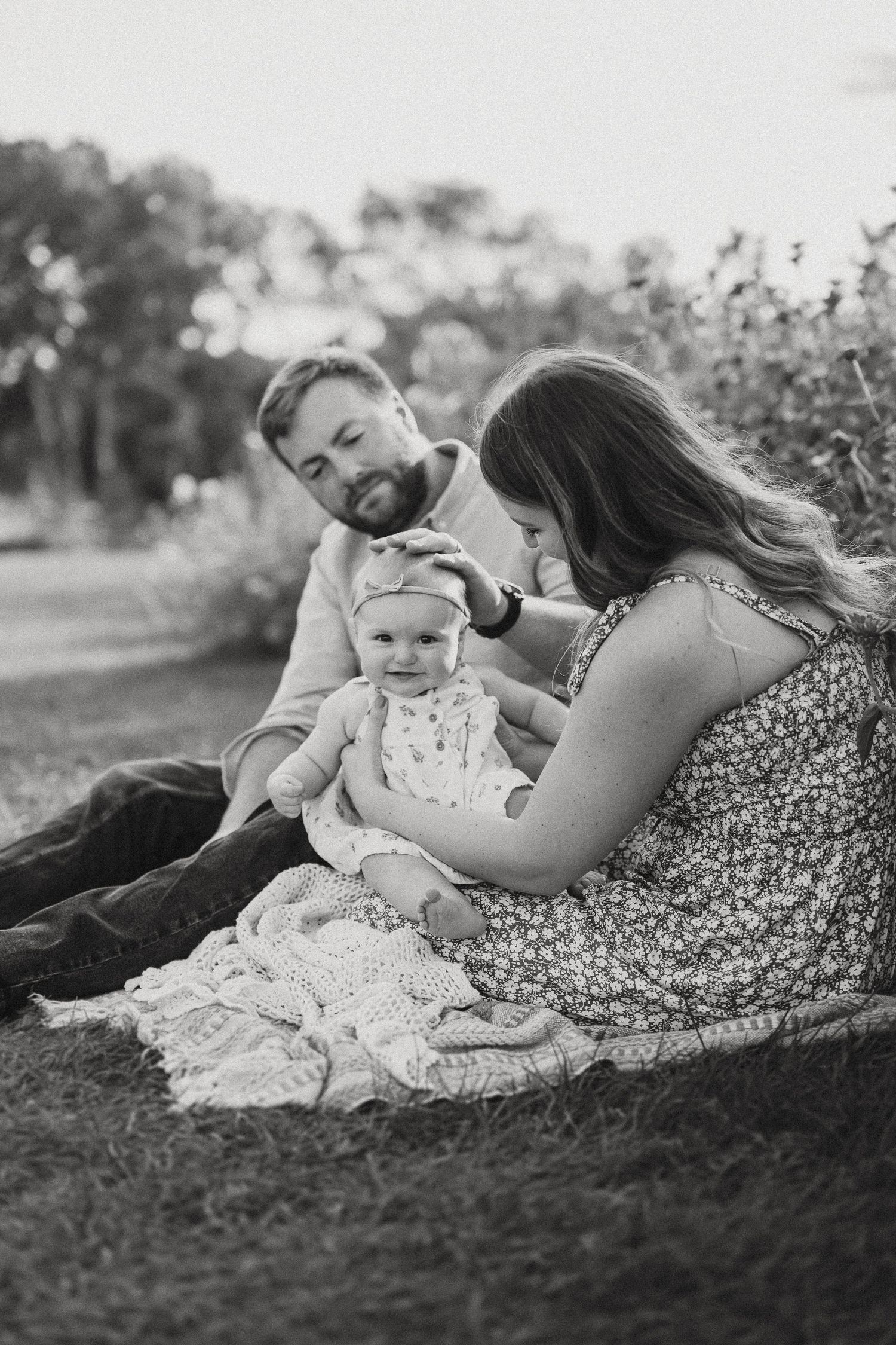 Black and white portrait of a family enjoying peaceful moments together on a blanket outdoors.