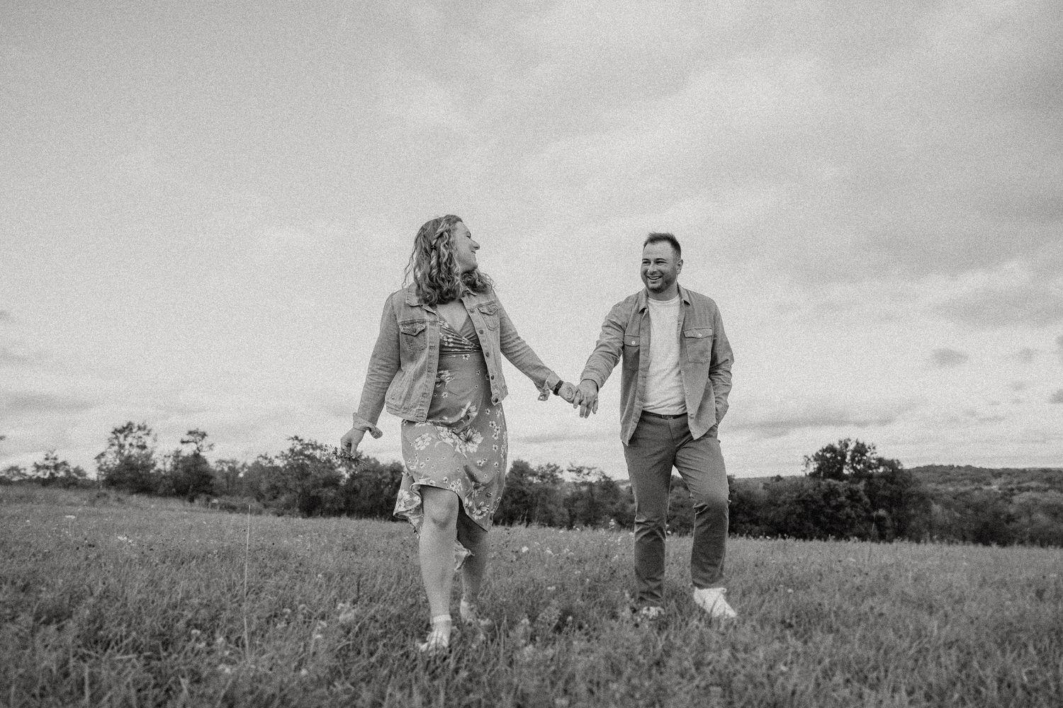 A couple holds hands while walking through a meadow in black and white.