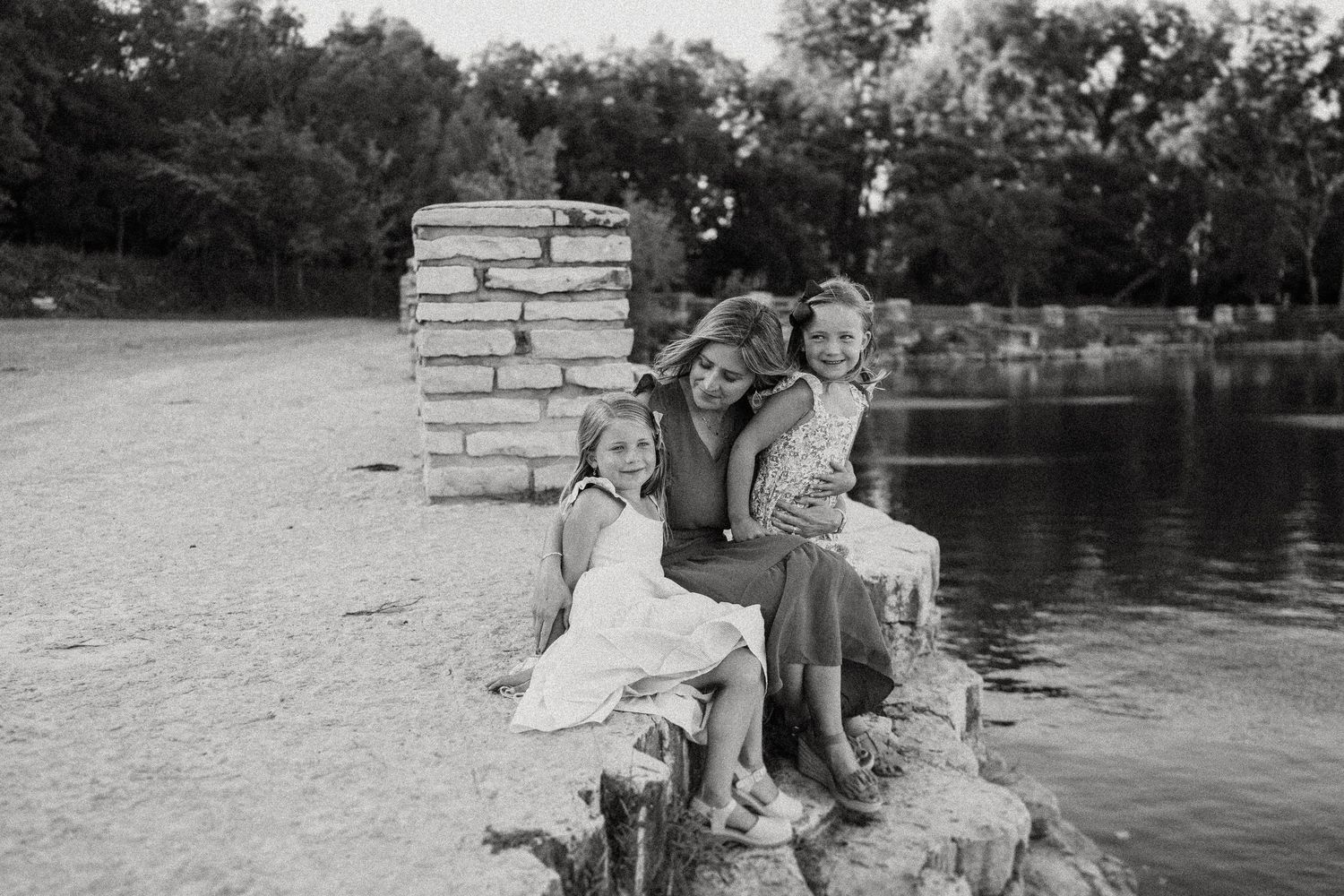 Black and white photo showing joyful expressions while sitting on stone blocks near a serene lakeside.