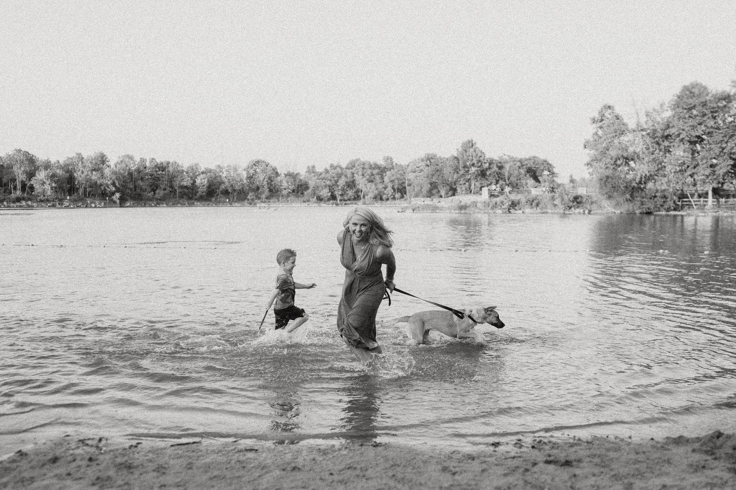 Black and white image of people enjoying the water at a tranquil lake surrounded by trees.