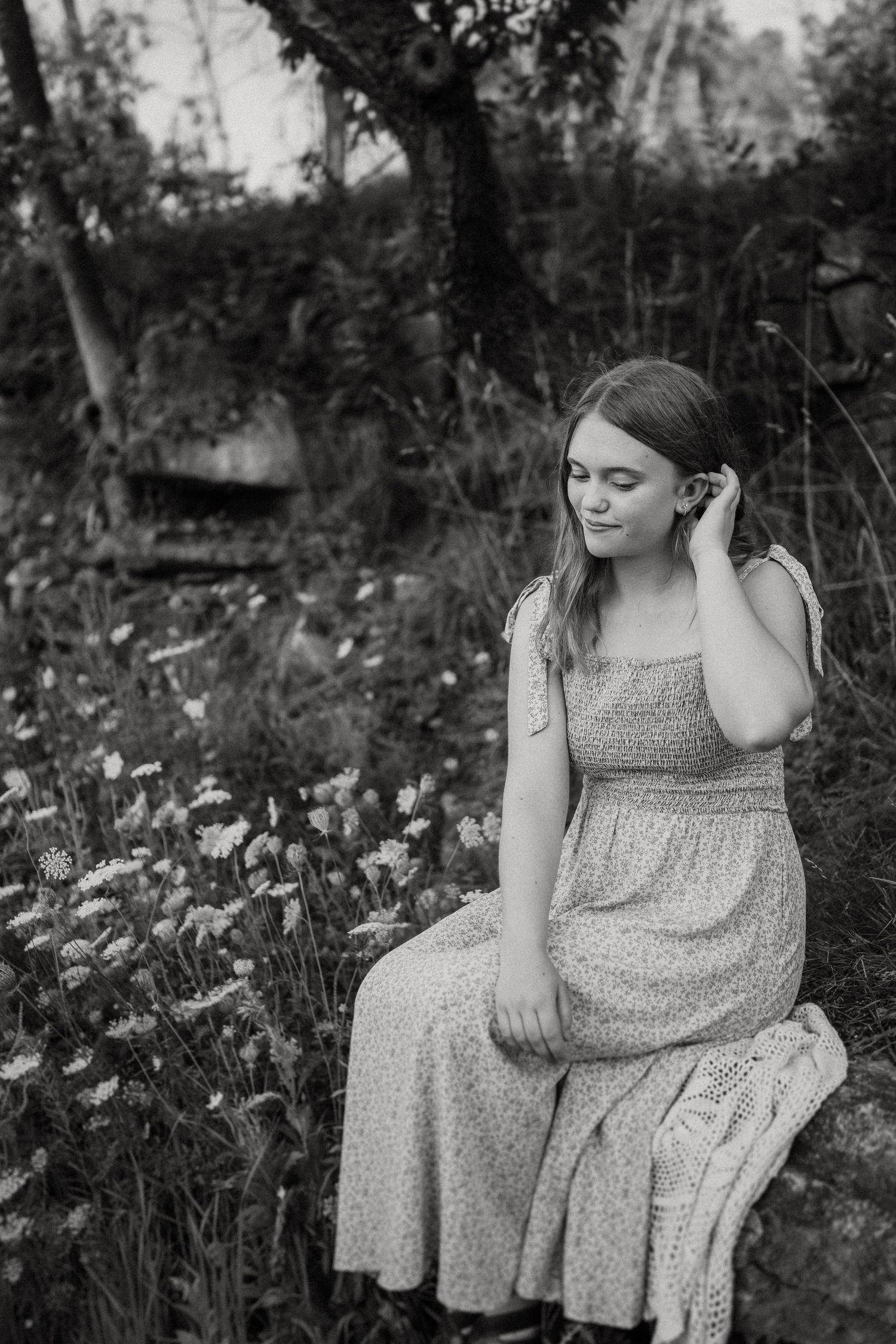 A black and white portrait showing a contemplative moment among wildflowers and natural scenery.