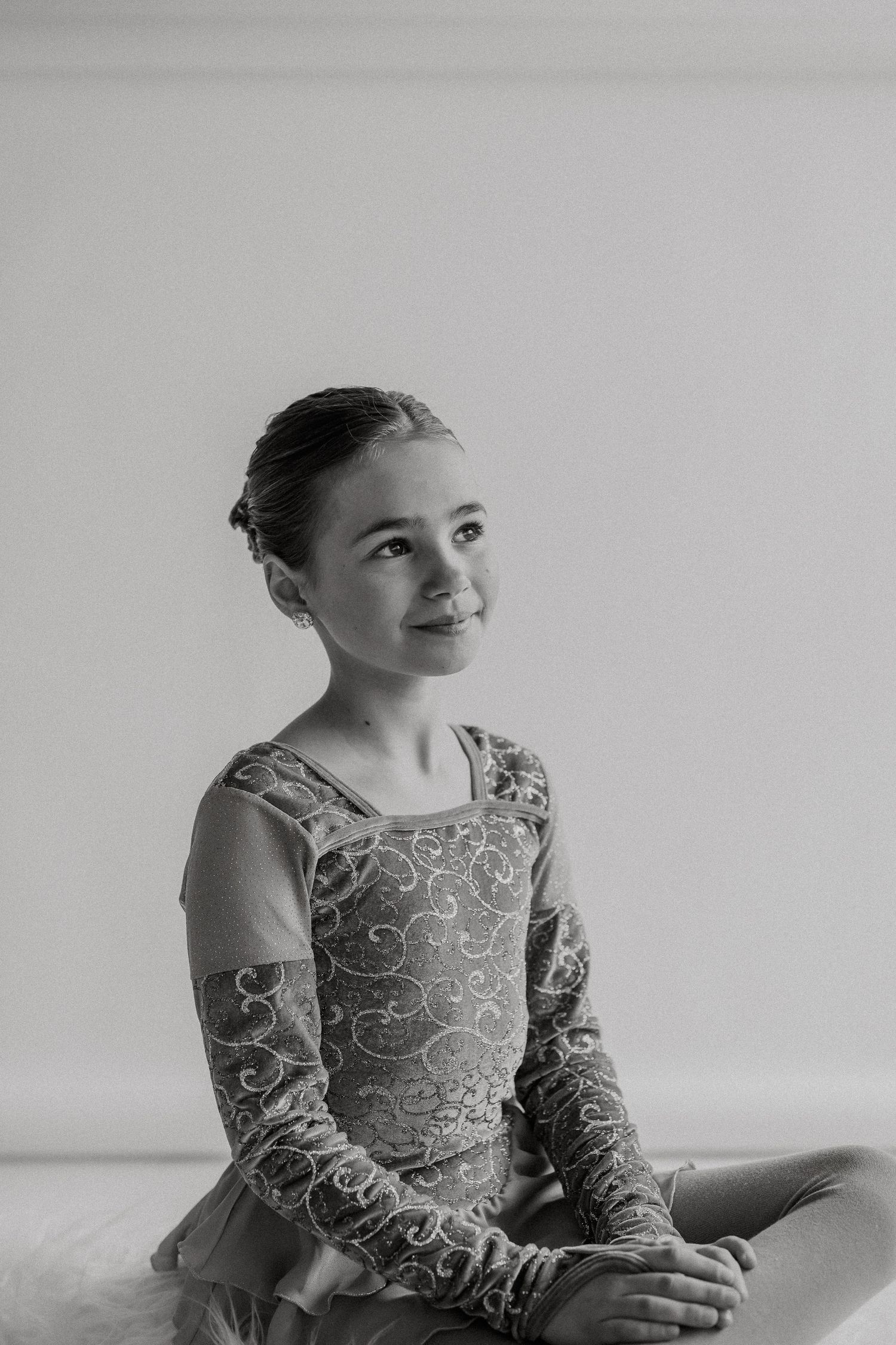 Young dancer in an elegant patterned leotard poses gracefully against a white background.