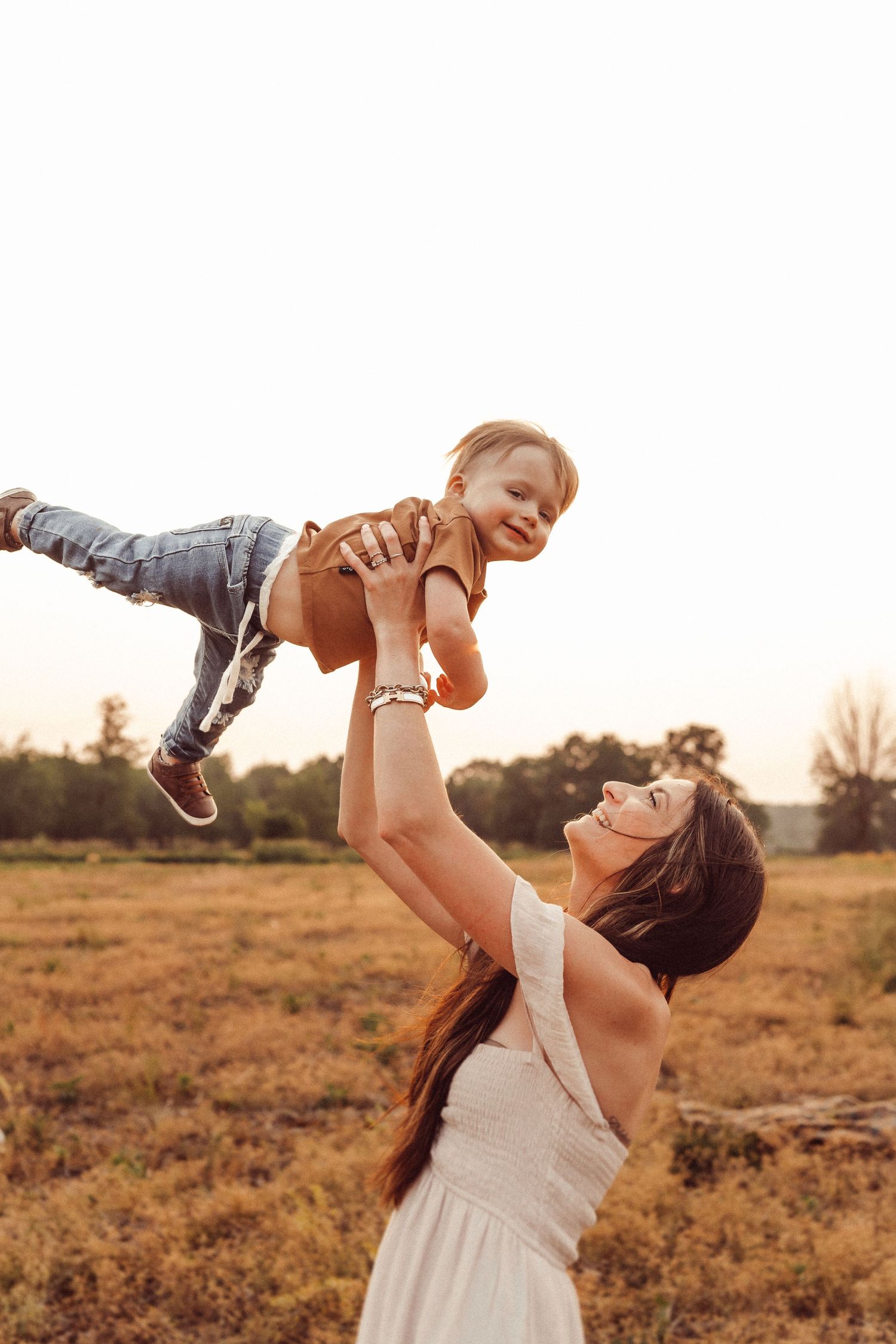 A joyful moment captured as a person lifts a small child high in the air at sunset.