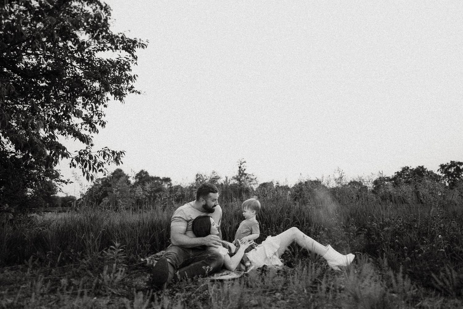 Black and white photo of a family relaxing together in a wild meadow.