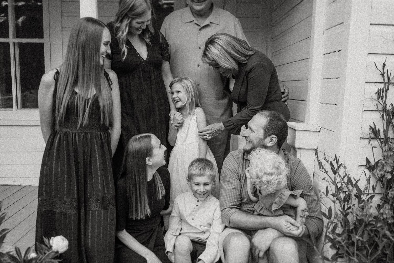 A black and white family portrait taken on rustic farmhouse porch steps.