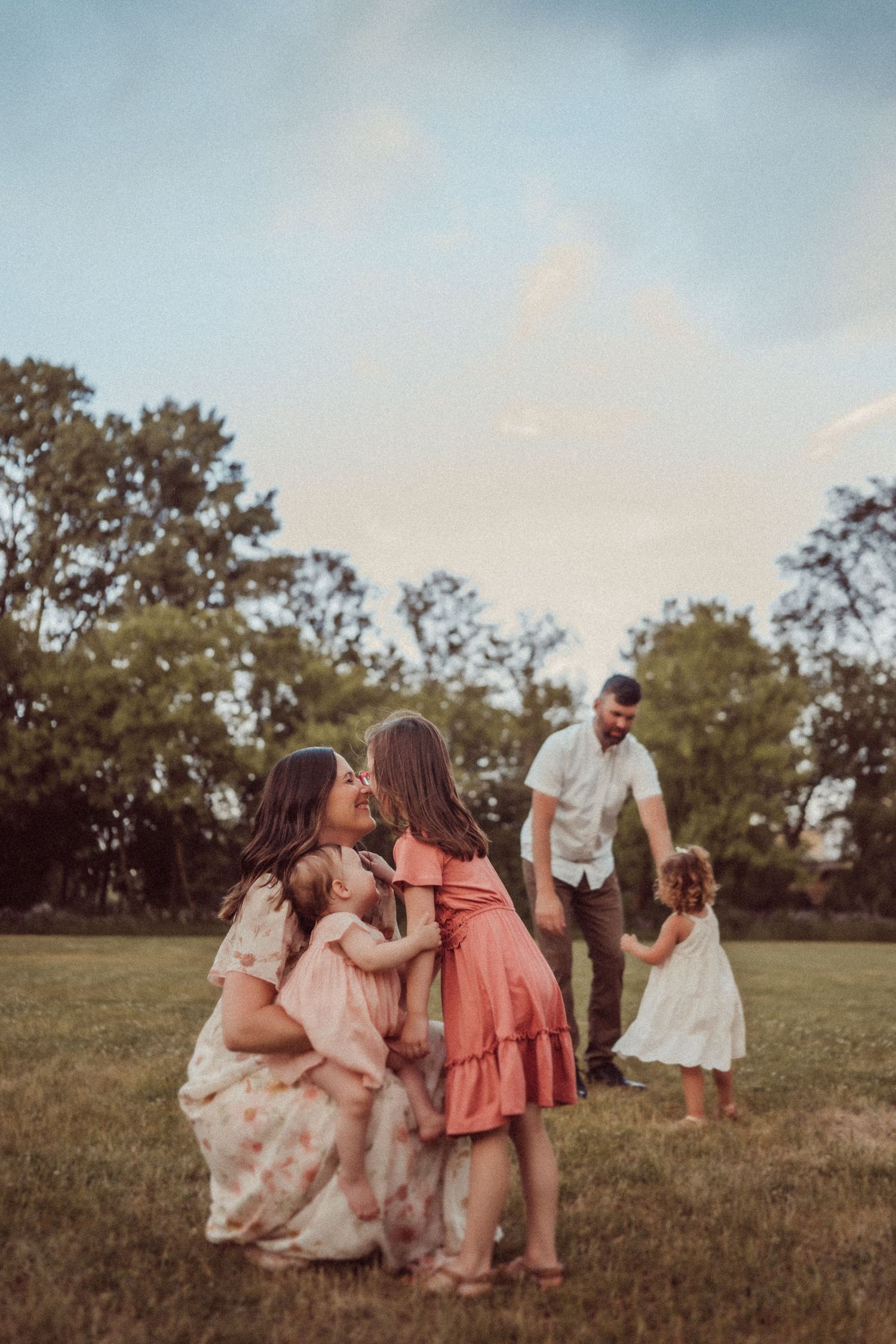 An intimate family moment captured during golden hour in a grassy field with trees in the background.
