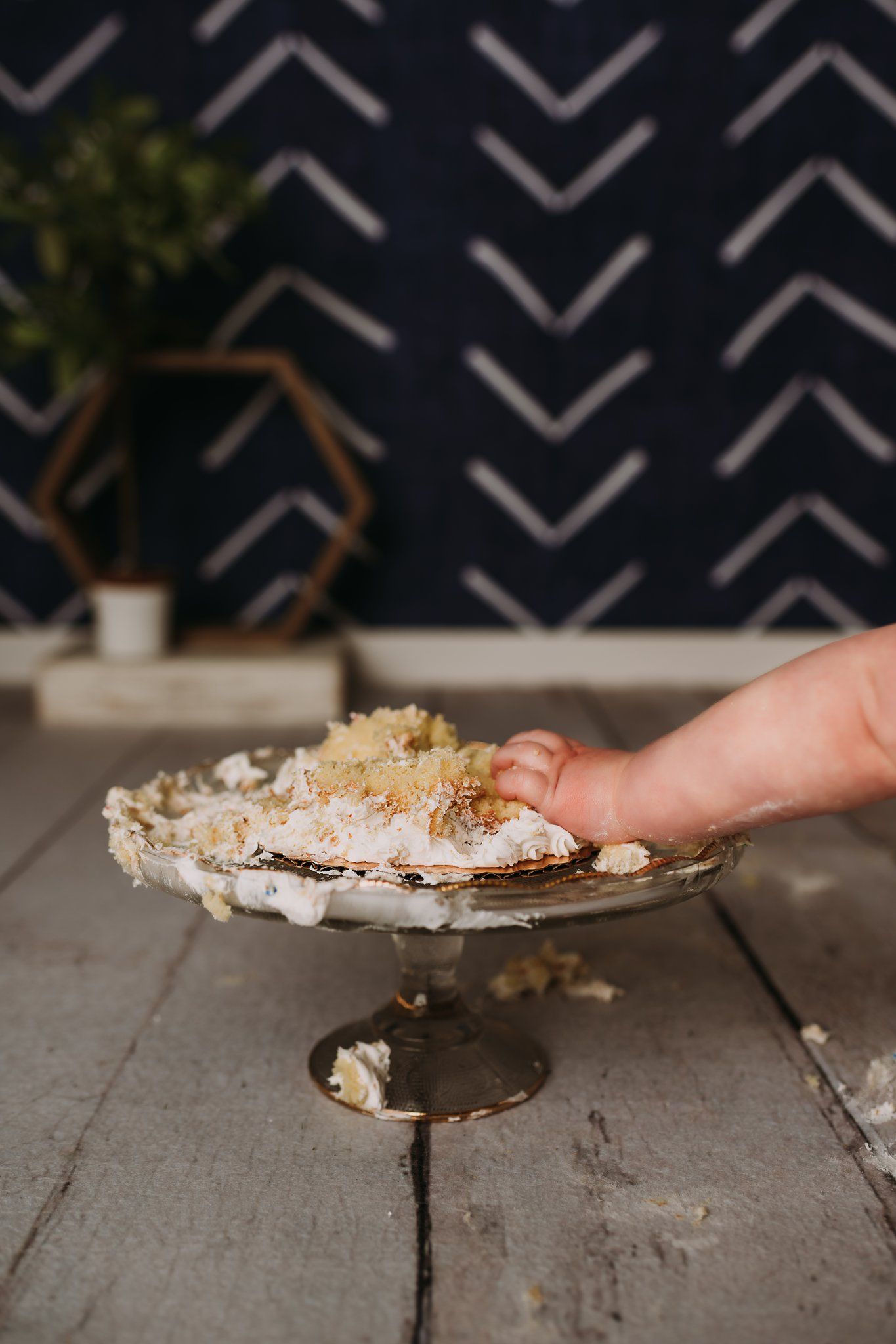 Half-eaten cake on silver pedestal plate sits on rustic wooden flooring.