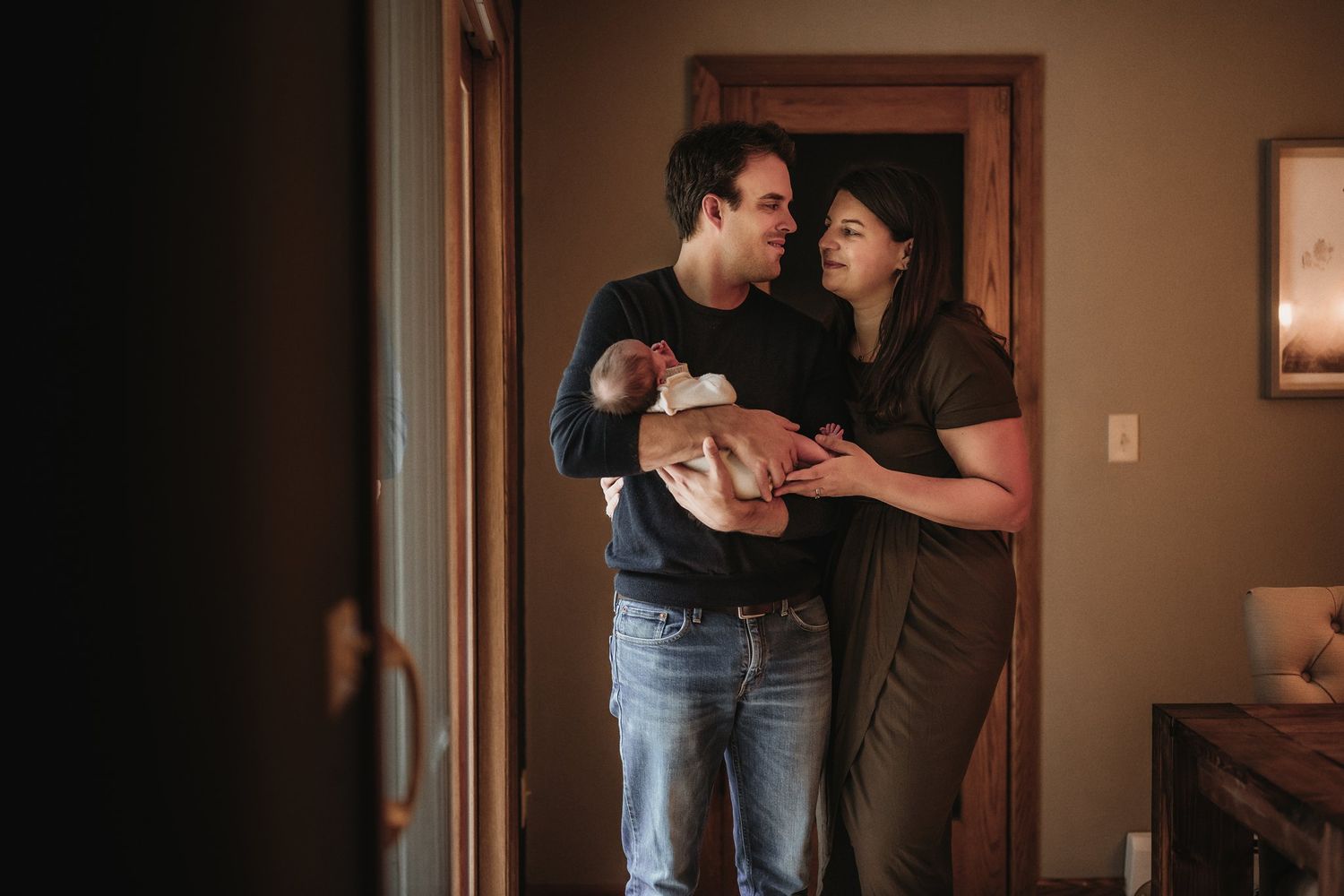 Parents share an intimate moment while cradling their newborn in their home.