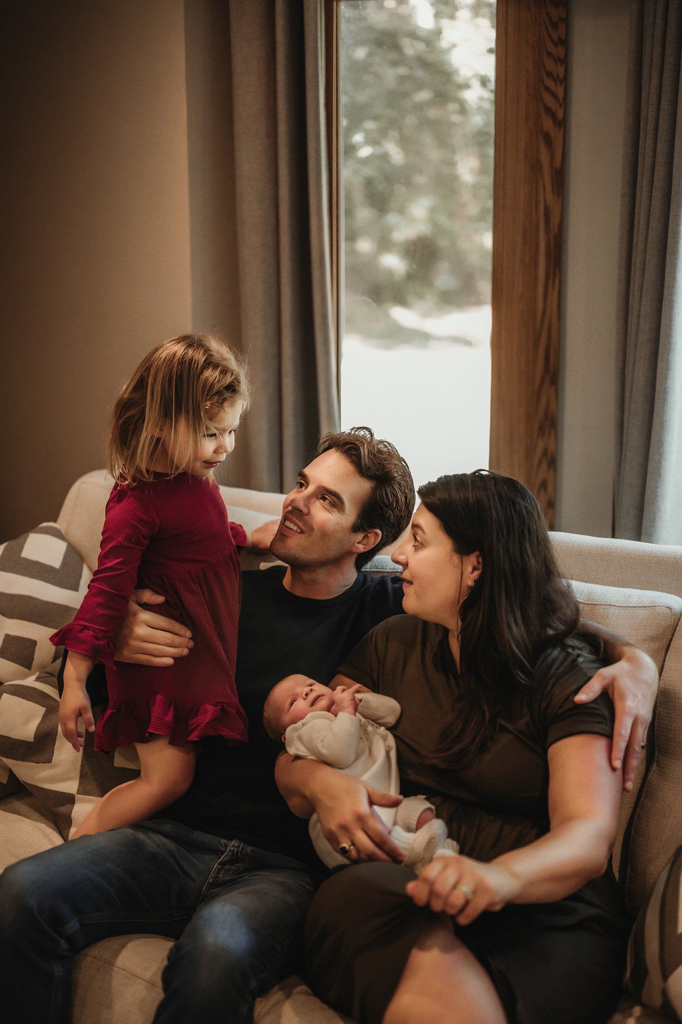A family shares an intimate moment together on their living room couch near a window.