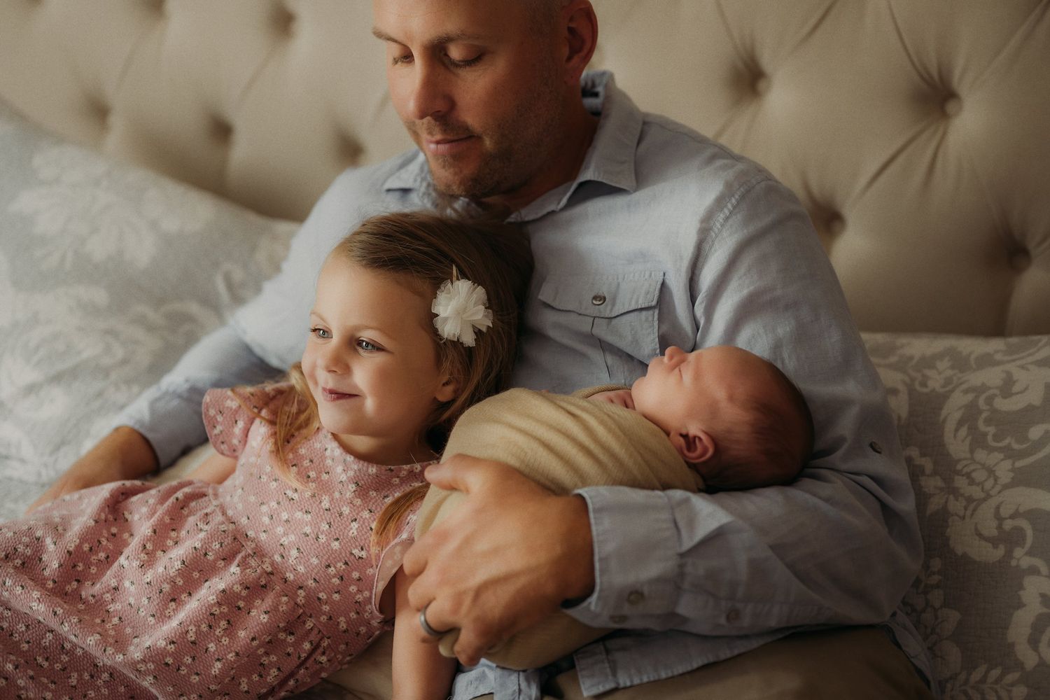 Intimate family moment captured on tufted headboard bed in soft lighting.