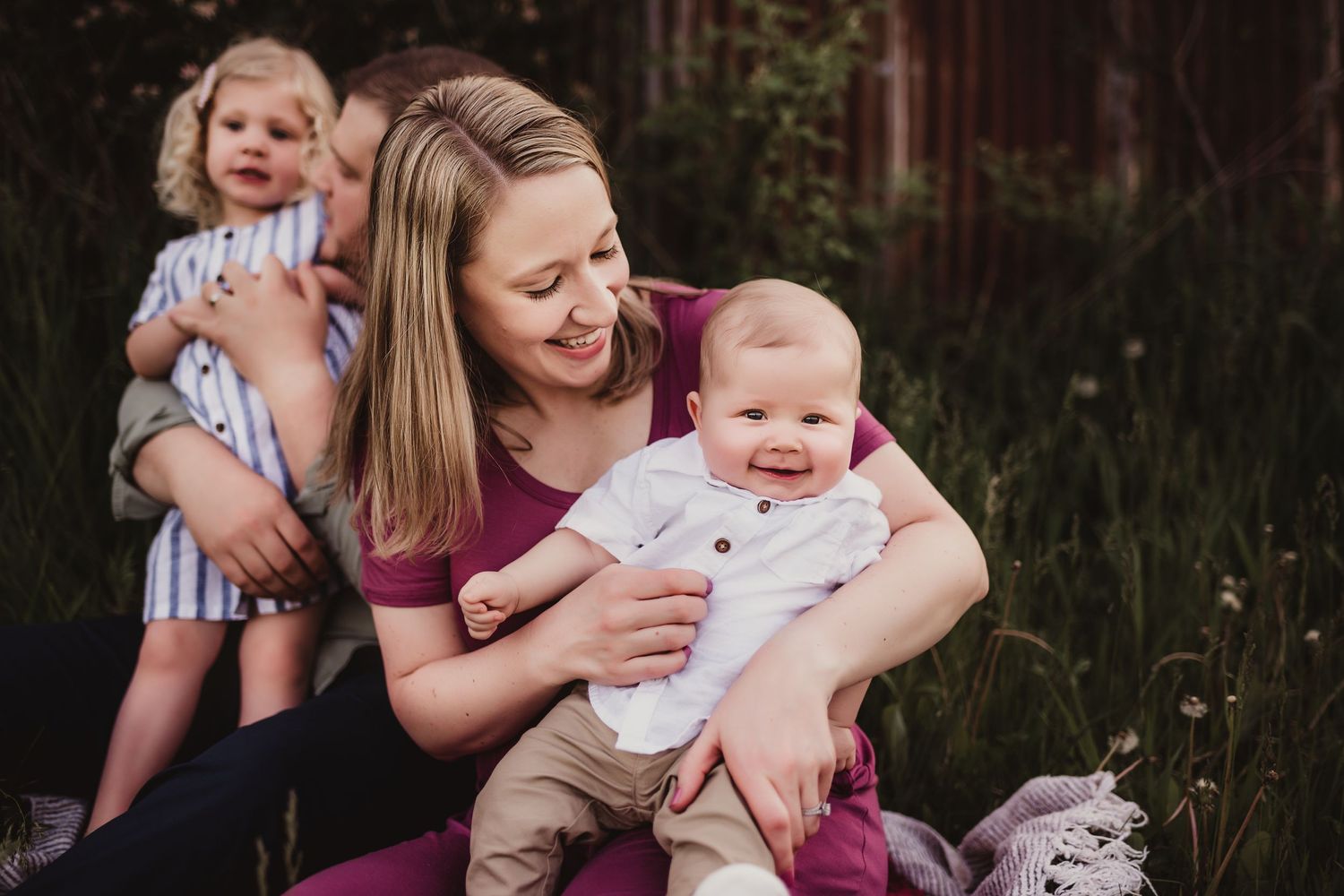 A tender family moment captured outdoors with a woman and children sitting in tall grass.