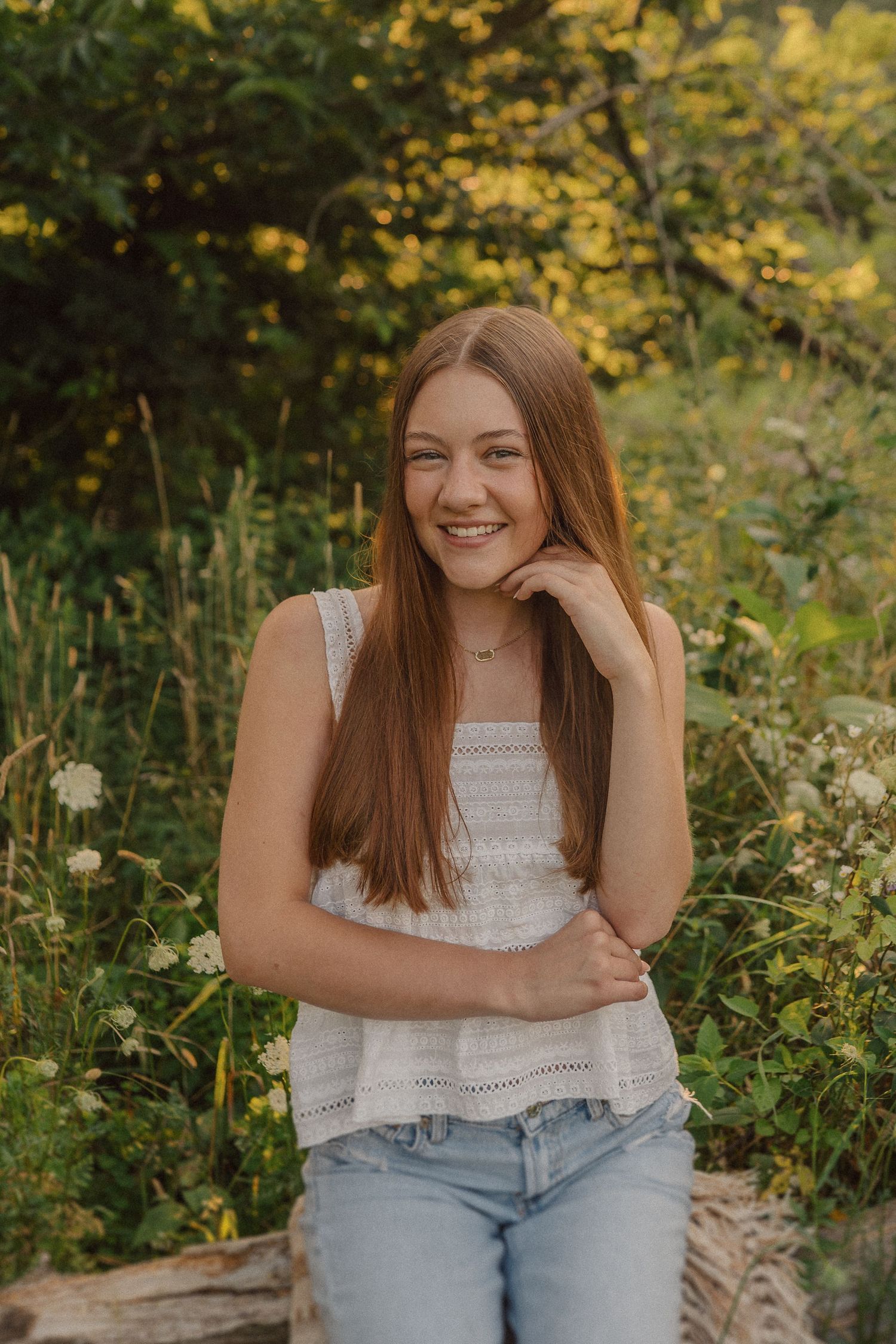 A person sitting in a natural setting with yellow wildflowers wearing denim and white lace.