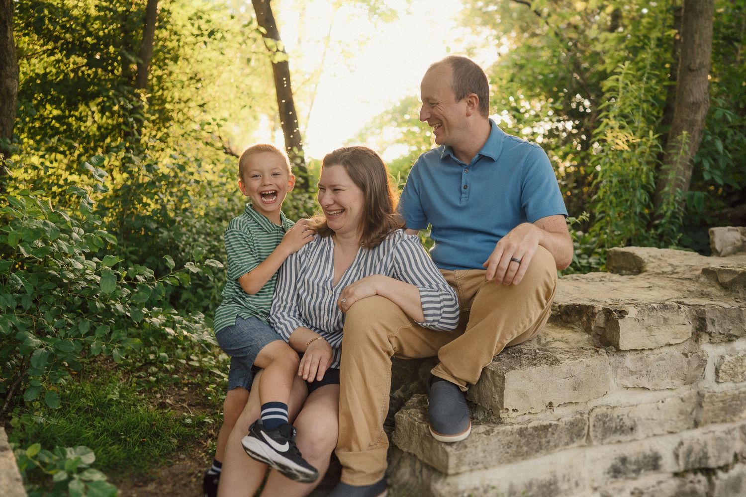 A family enjoying a playful moment together while sitting on stone steps in a lush outdoor setting during golden hour.