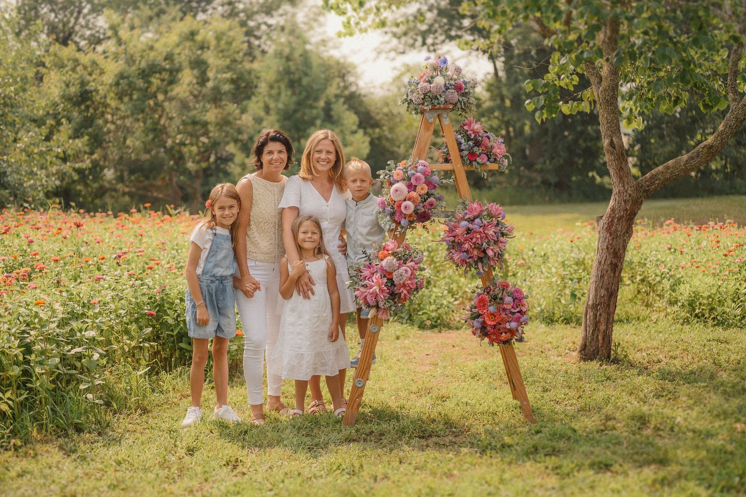 Family portrait session in a sunny garden with a wooden arch adorned with pink and purple flowers.