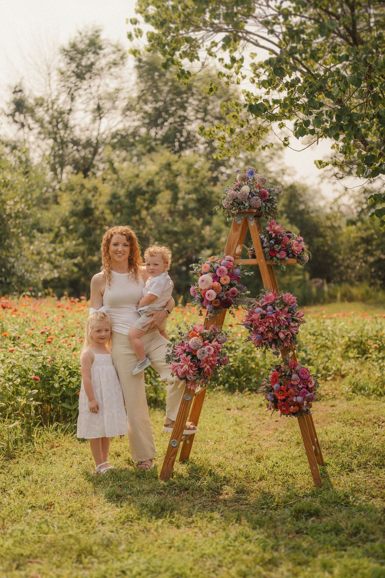 Outdoor photoshoot scene with a wooden ladder decorated in pink and purple florals against a natural backdrop.