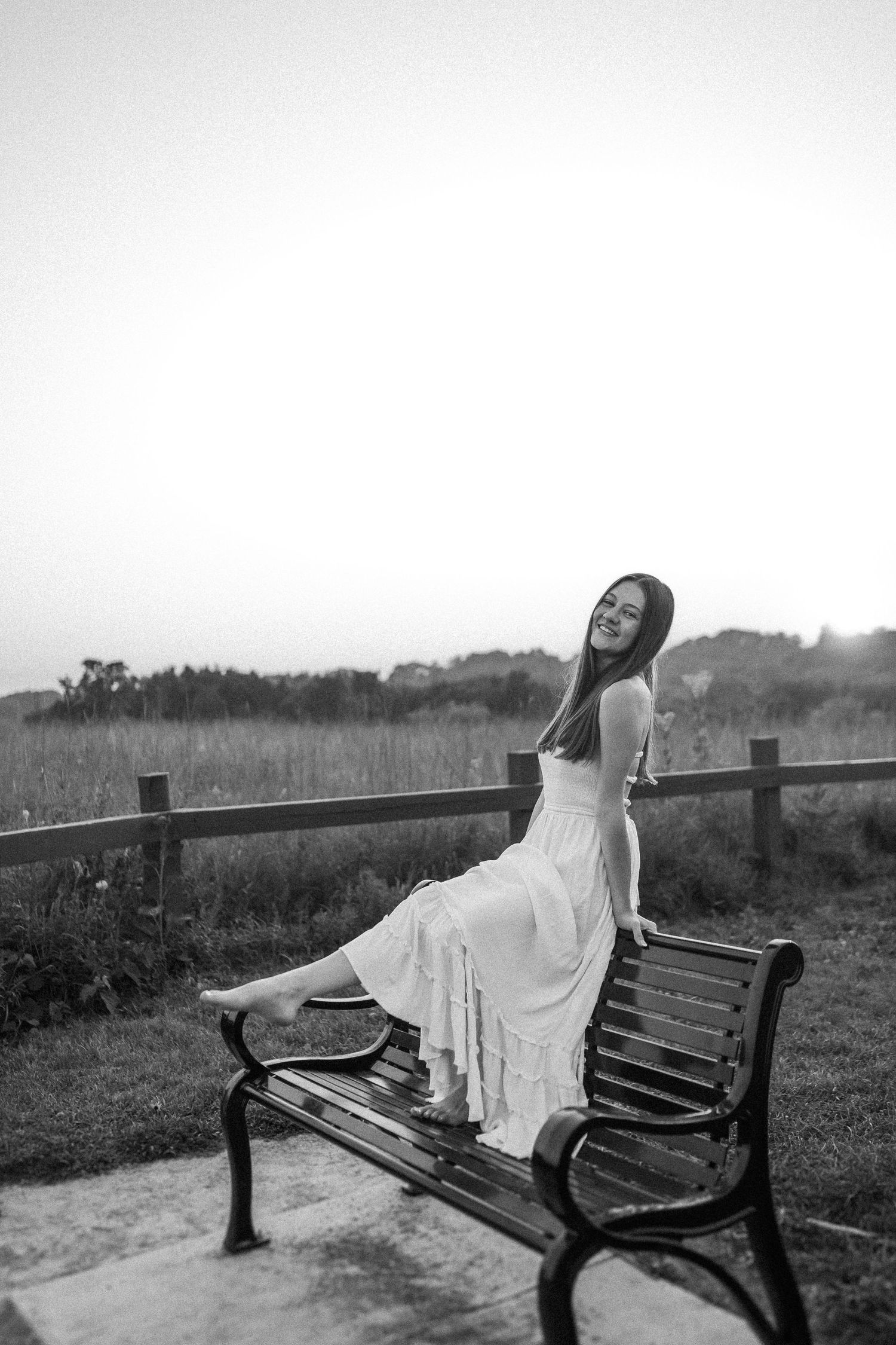 A dramatic black and white portrait of someone posing on a park bench at dusk.