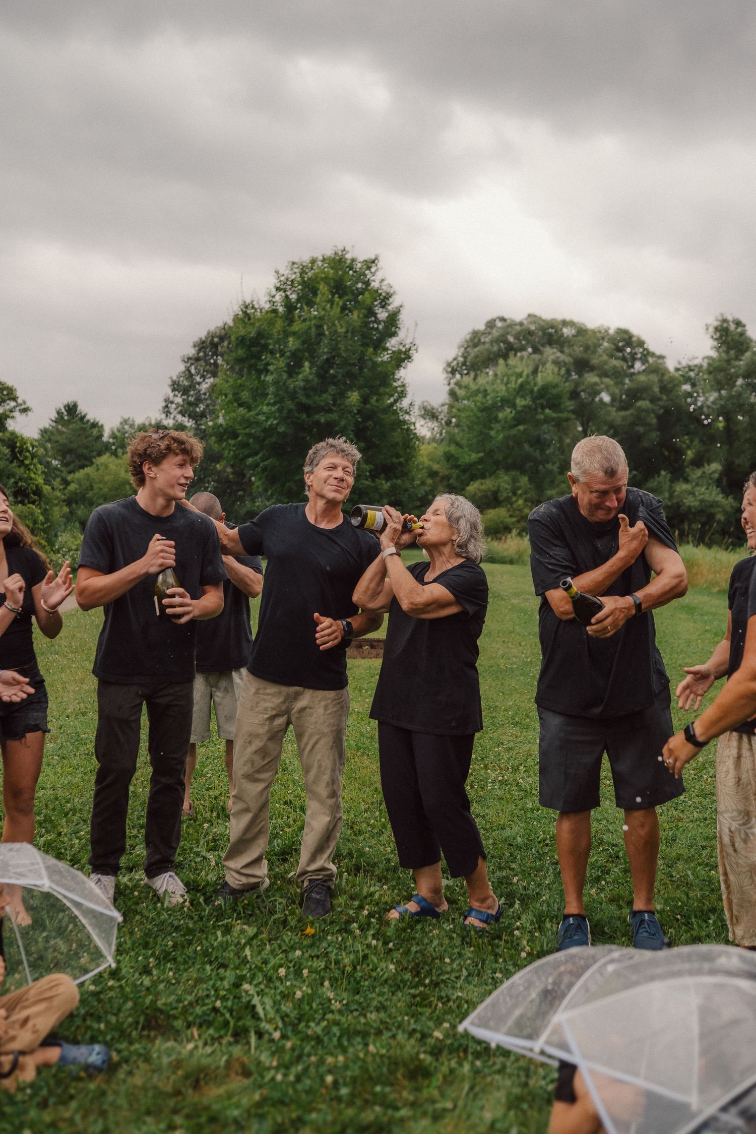 Family members in black outfits splash water and laugh together during outdoor photo shoot.