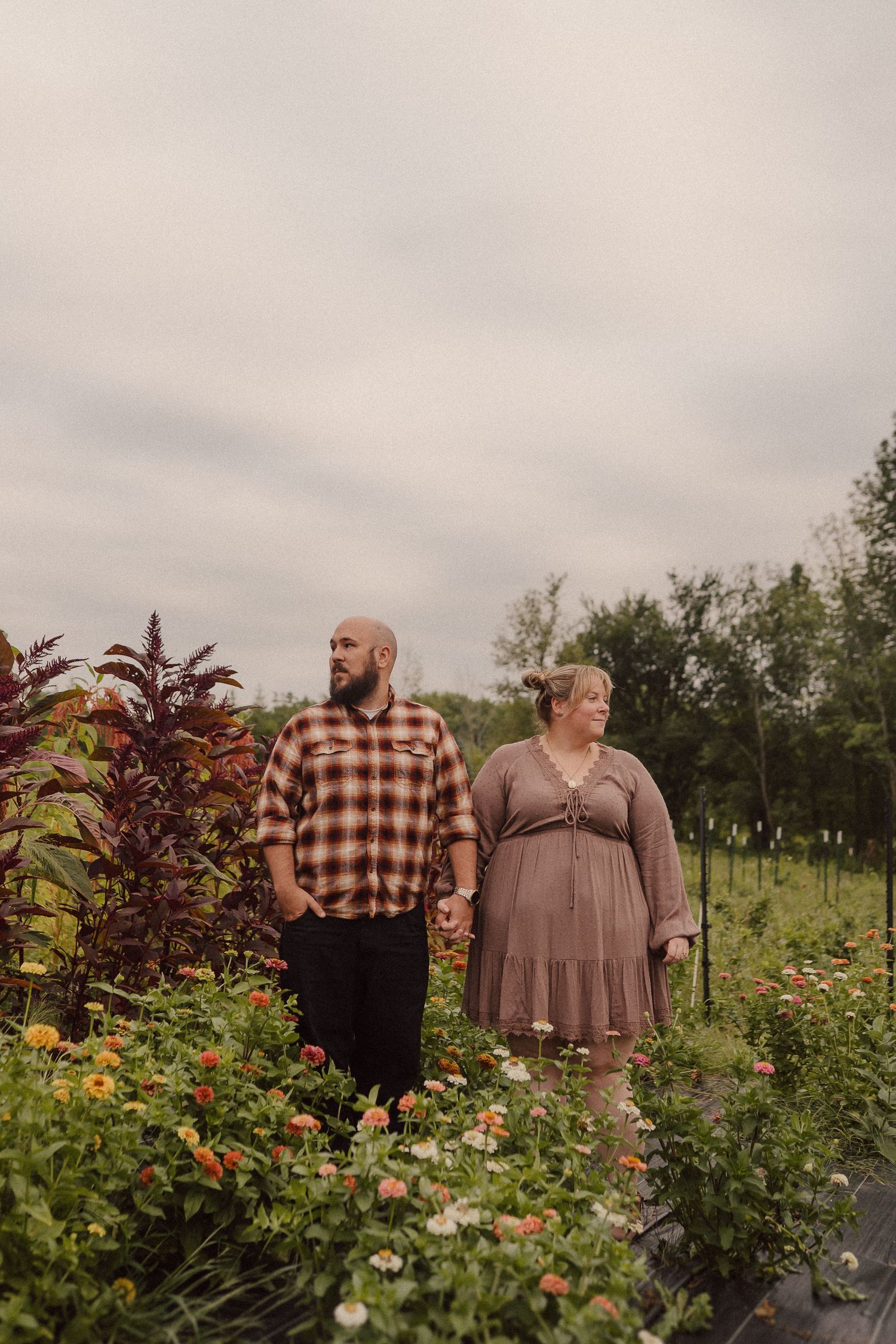 A couple strolls through a colorful garden filled with blooming flowers on an overcast day.