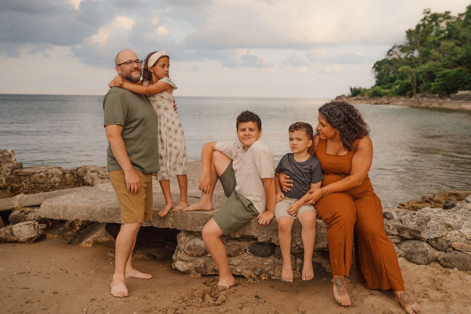 A group sits together on rocky beach terrain at sunset by the ocean's edge enjoying a relaxed moment.