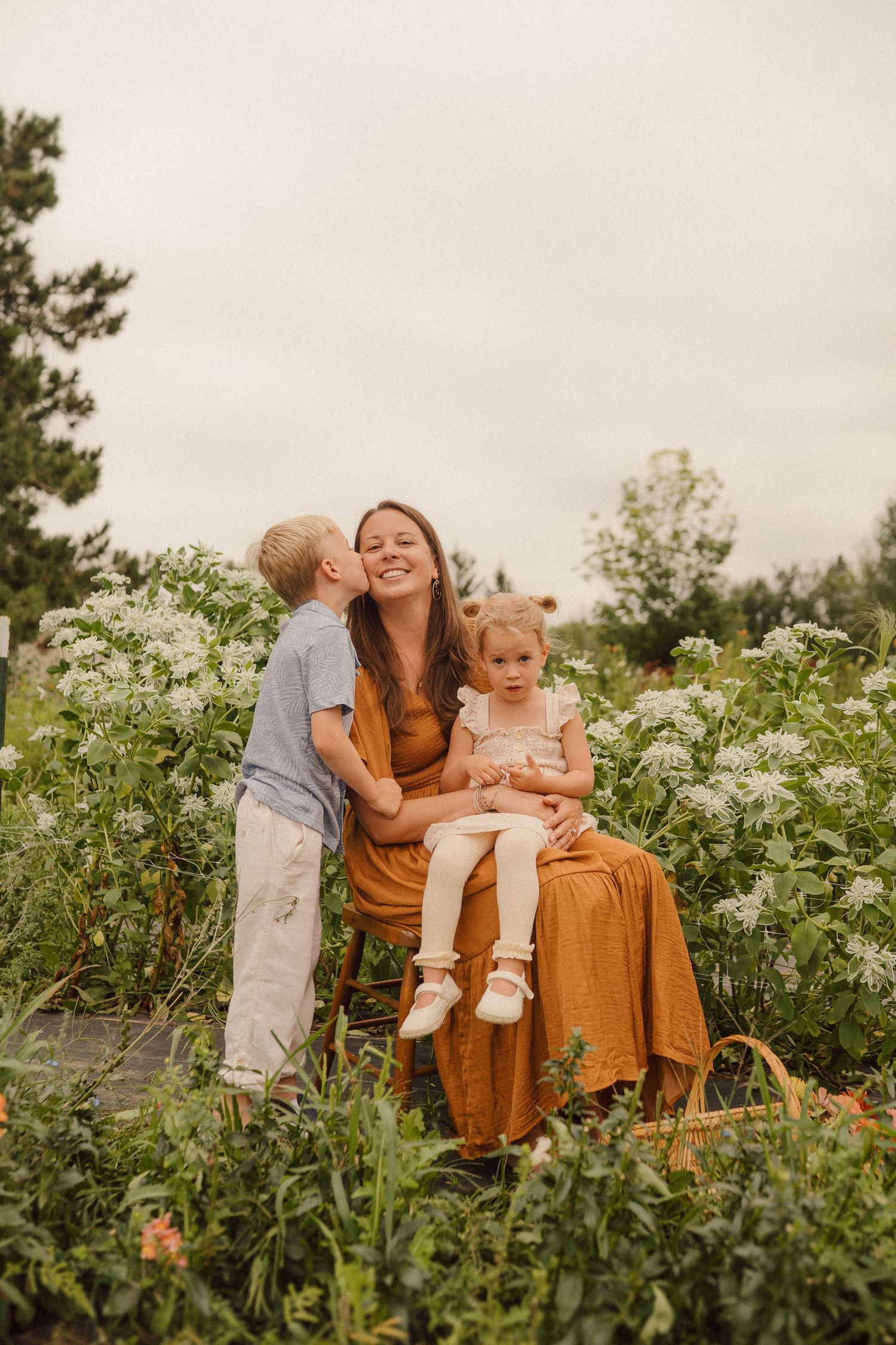 Family sitting together in a blooming wildflower field with green foliage and white flowers on an overcast day.