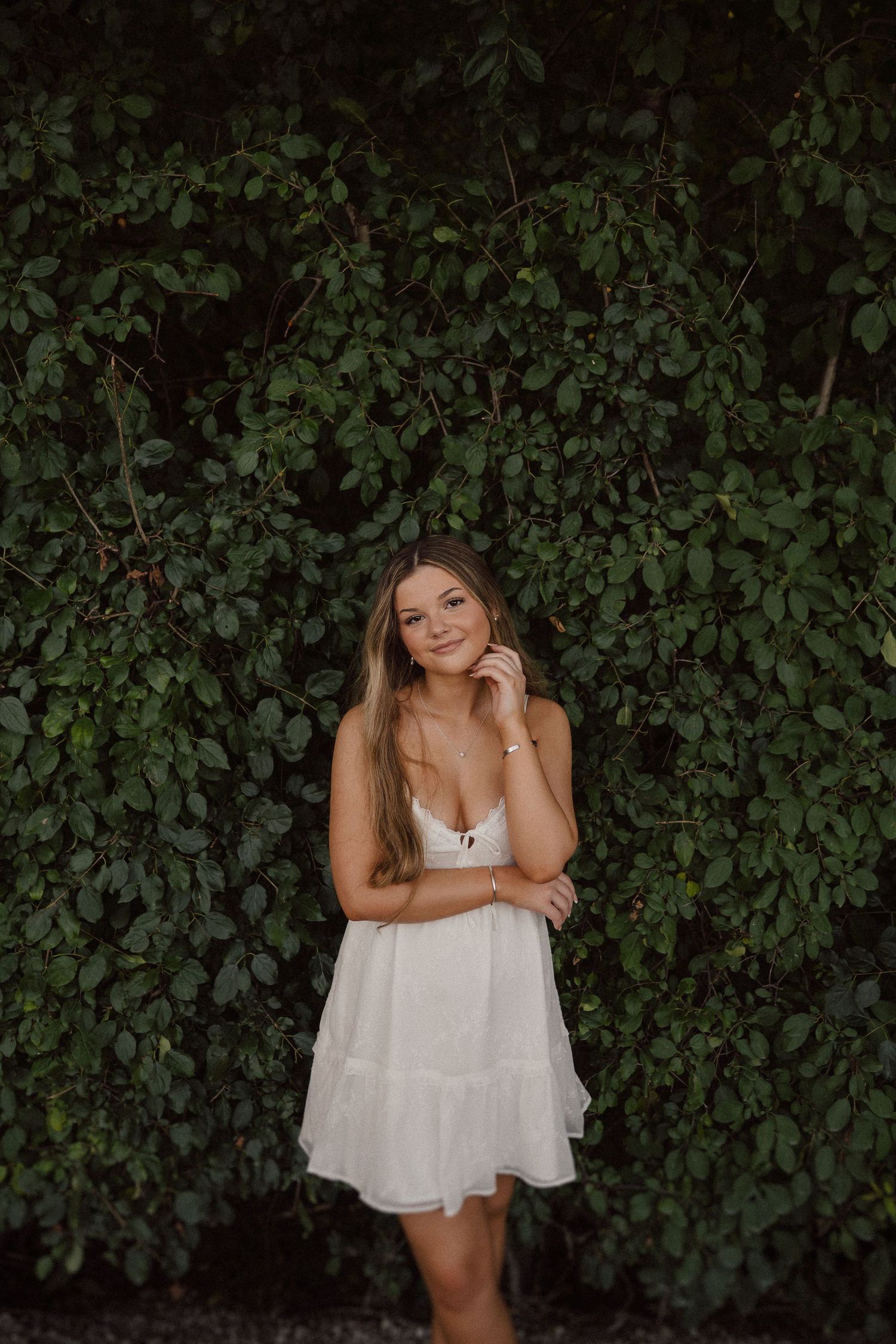 Outdoor portrait against a dark green wall of foliage and ivy.