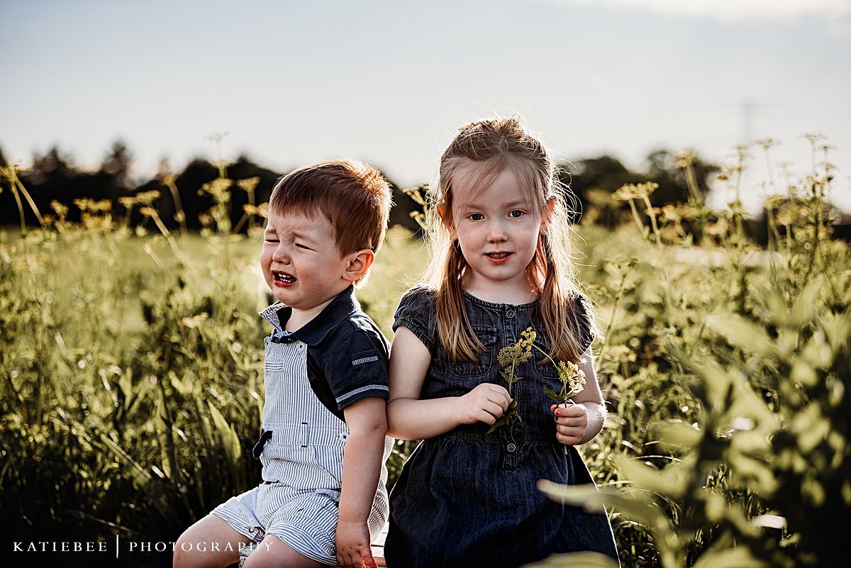 Two children in coordinating navy outfits playing together in a wildflower field.