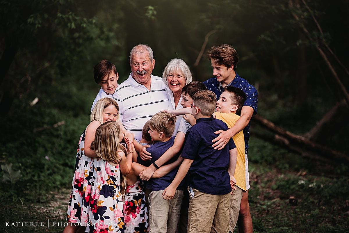 Candid multi-generational family photo showing playful interaction in a wooded setting.