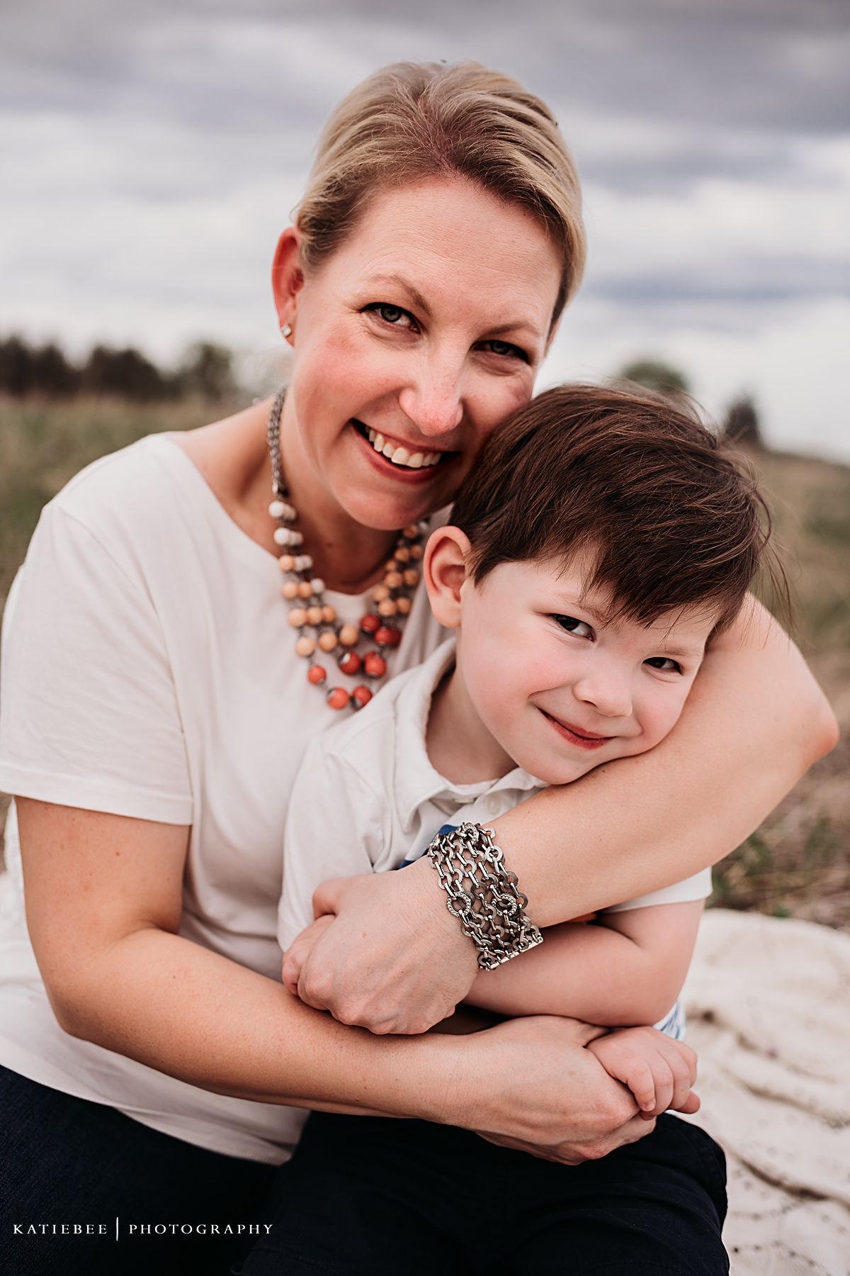 A sweet moment between parent and child embracing outdoors against a moody sky backdrop.