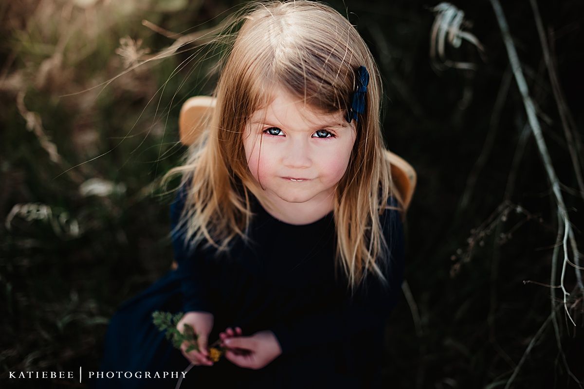 Close up portrait of child in black sweater against natural backdrop.