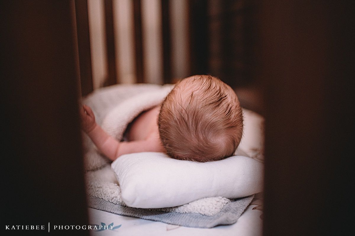 Close-up view of an infant resting on soft white bedding in dim lighting.