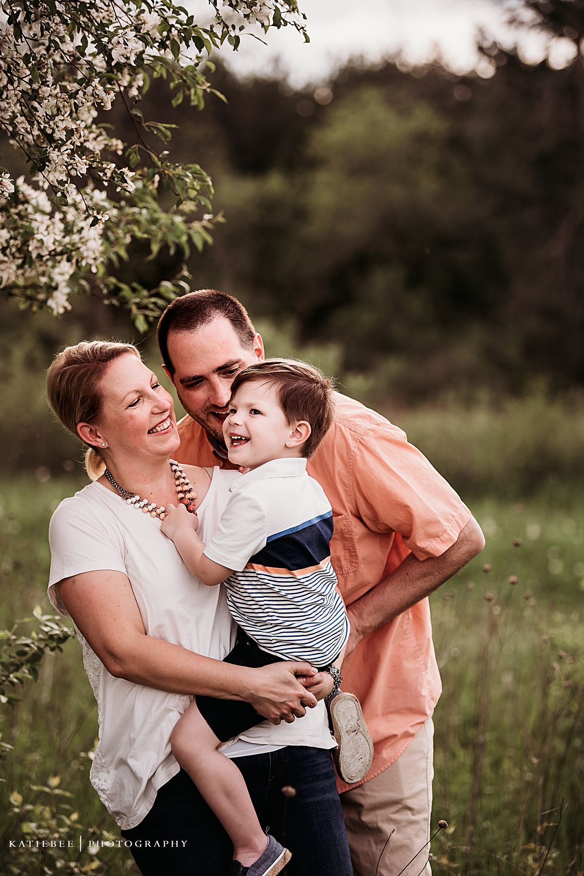 A joyful family moment captured outdoors in nature with soft lighting and blooming flowers.