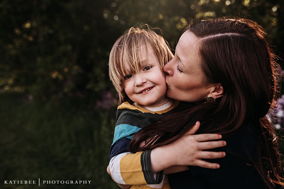 Tender moment captured between parent and child against a natural outdoor backdrop.