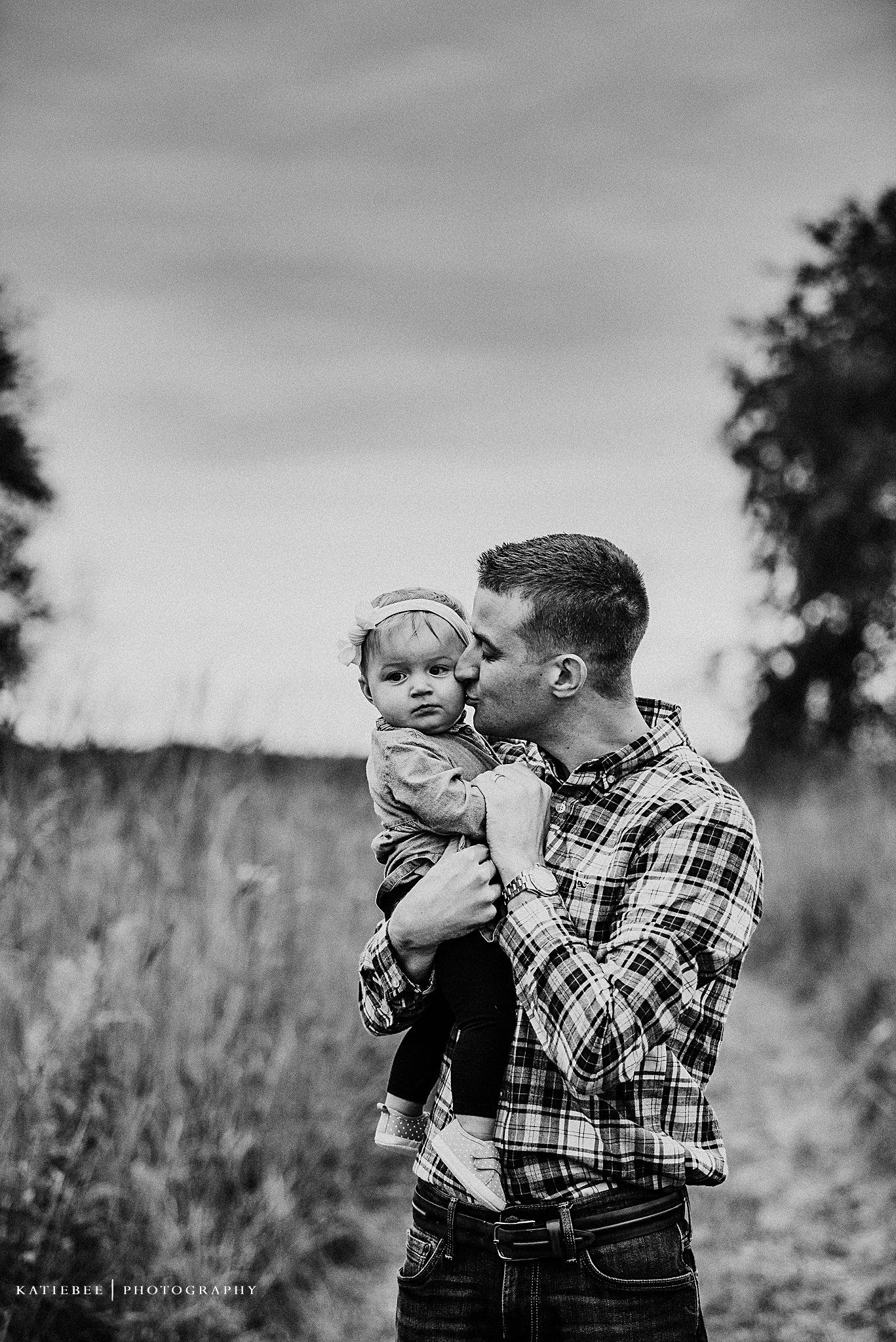 Intimate black and white portrait of father and child moment in tall grass field.