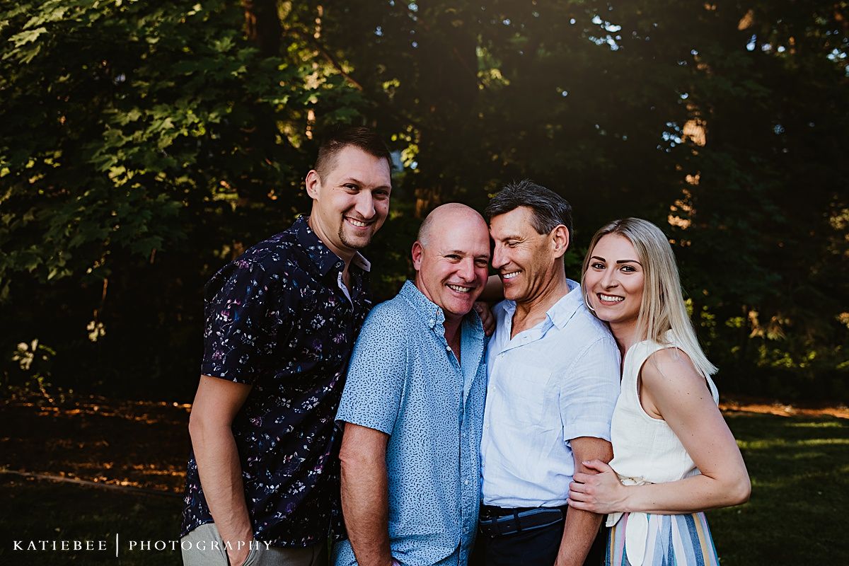 Four people pose together for a portrait in a sunlit wooded area.