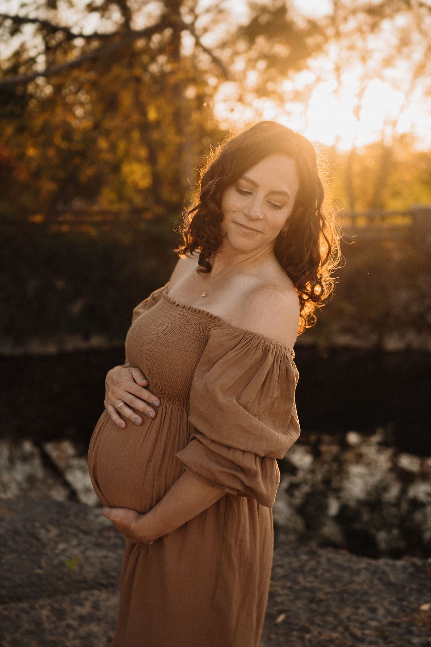 Glowing maternity portrait of woman in brown dress during golden hour.