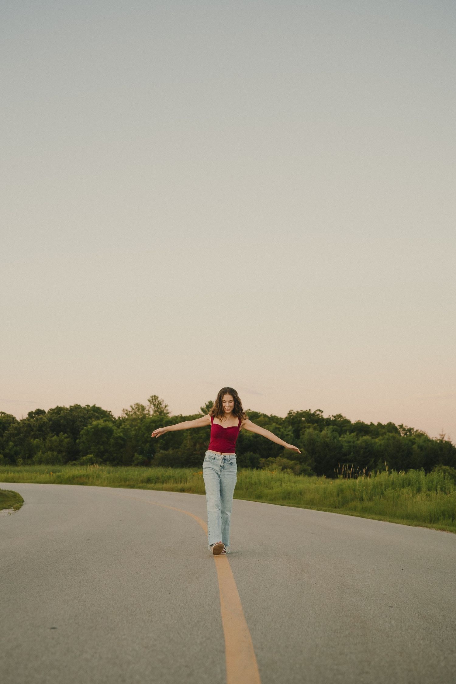 A playful pose on a country road shows someone balancing with arms outstretched at dusk.