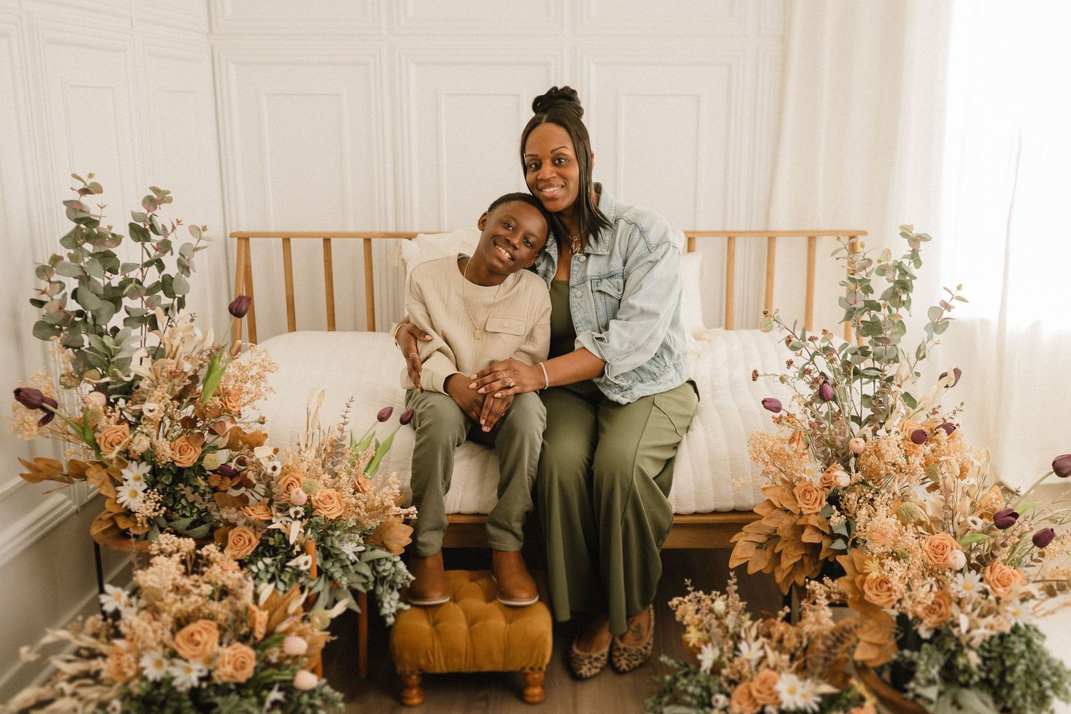 Two people sitting on wooden bench surrounded by beautiful peach and coral floral arrangements in a bright white room.