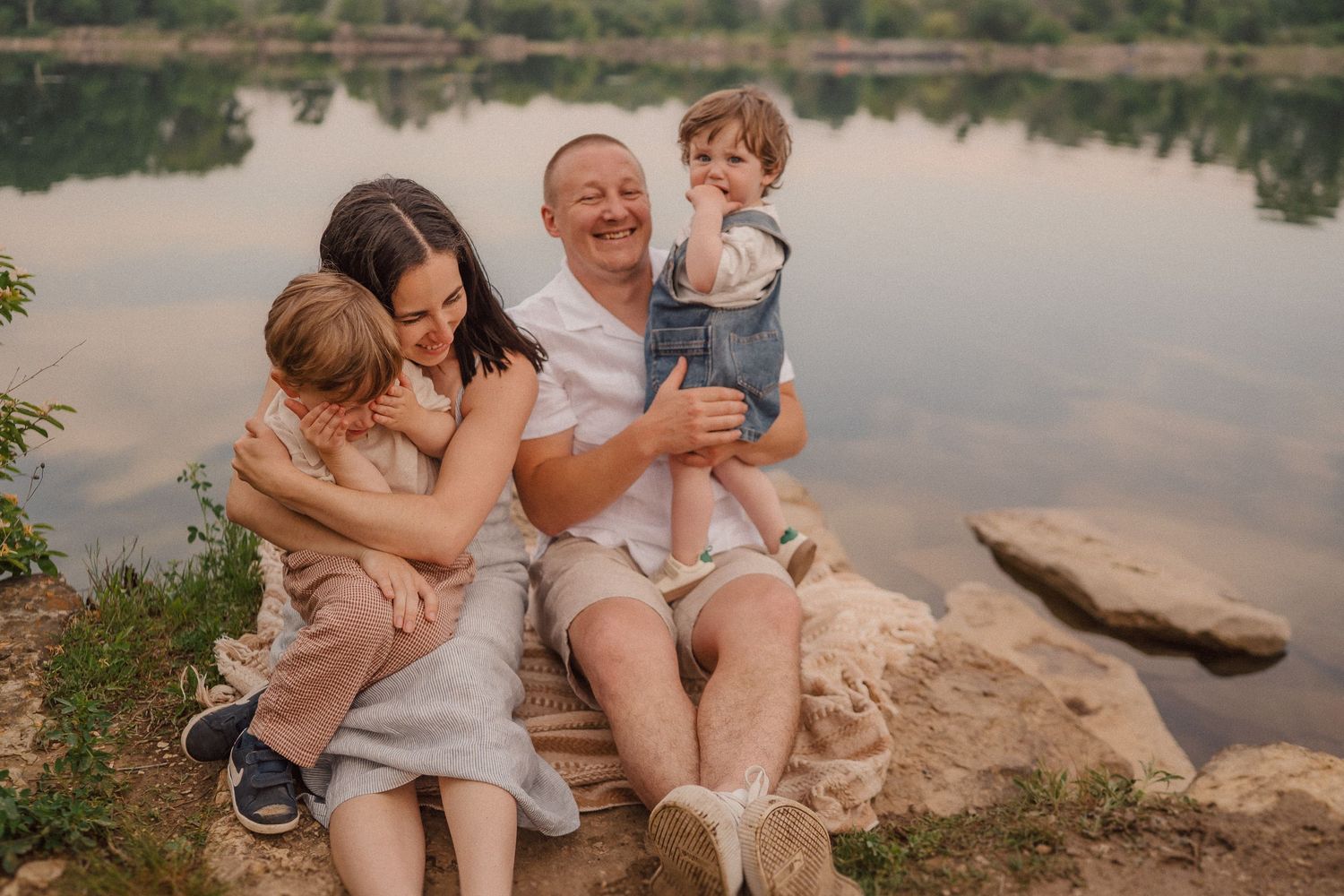 Family group sitting together on natural riverbank during golden hour.
