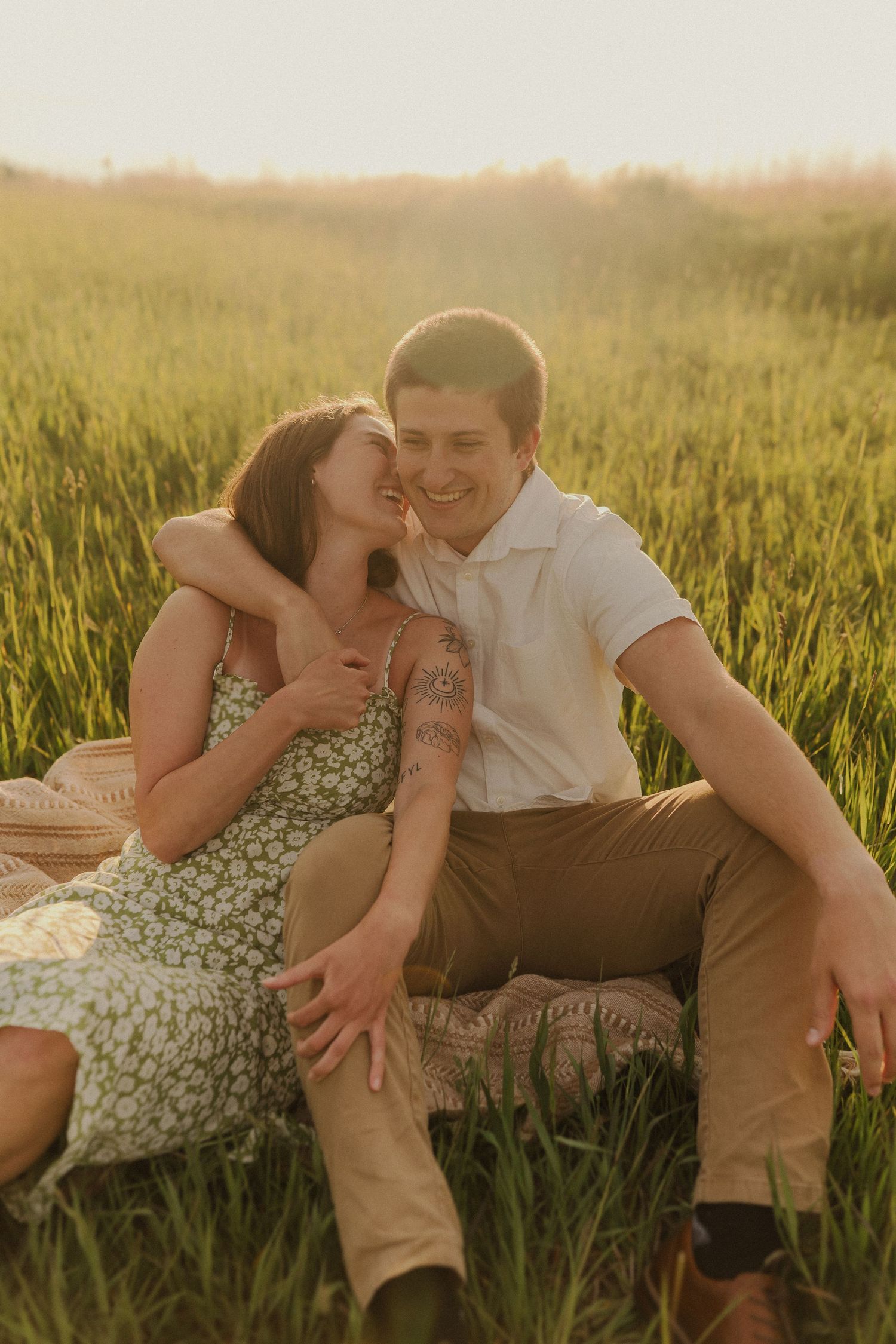 A loving couple shares a tender moment while sitting on a blanket in a sunny wheat field at golden hour.